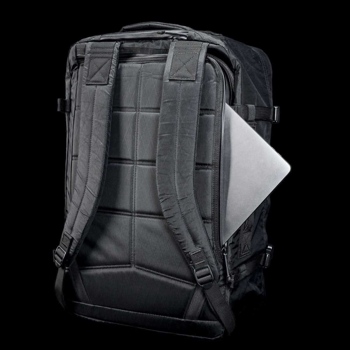 The GR3 - X-PAC, a black waterproof carry-on backpack, features a silver laptop partially tucked into its back pocket, shown against a black background.