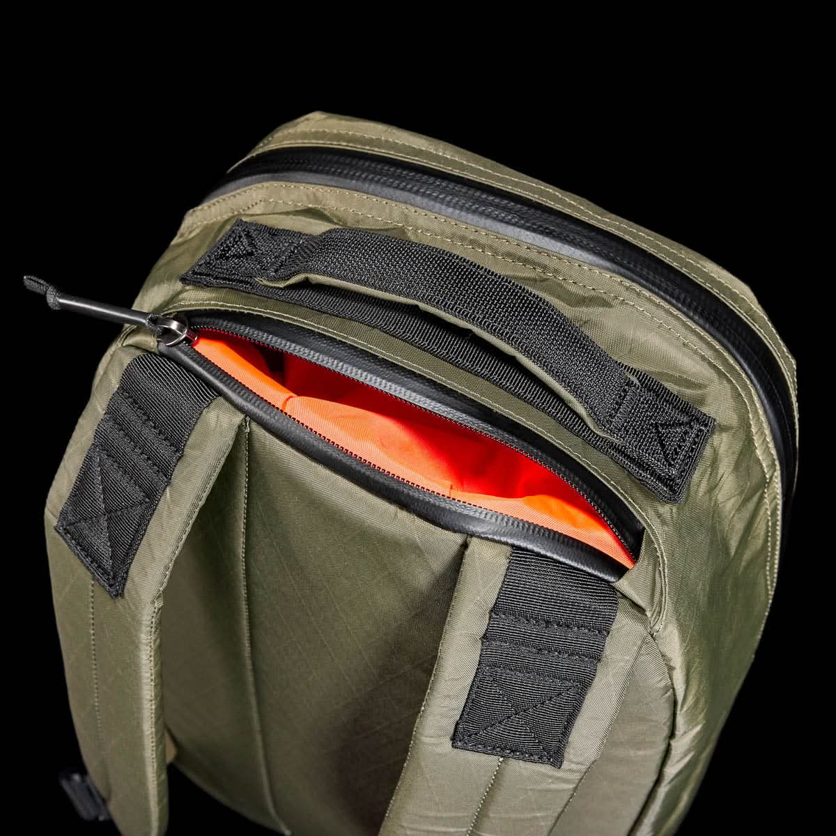 Top view of the Bullet X-PAC daypack in olive green with black straps, a bright orange interior, and AquaGuard zippers, shown unzipped.