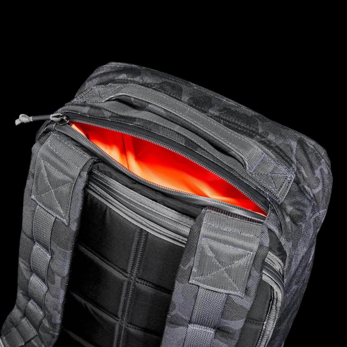 Close-up of black GORUCK rucksack with padded straps and bright orange interior lining against black background