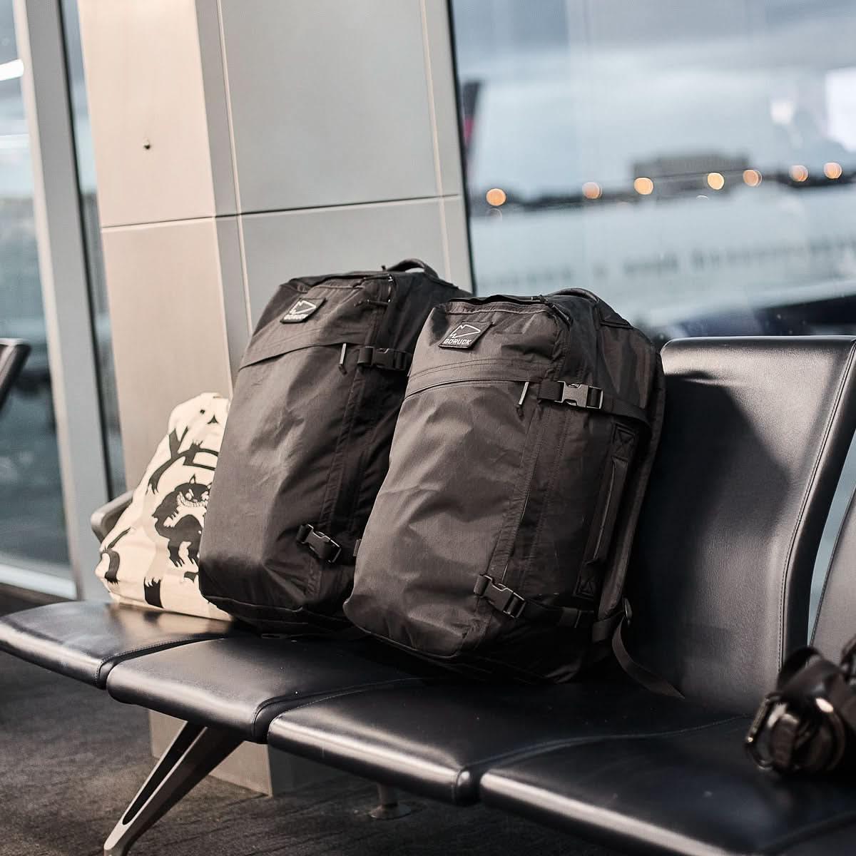 Two GR3 - X-PAC black carry-on backpacks sit on airport seats. Made from waterproof material for any journey, they combine reliability and style—plus each is backed by the Scars Lifetime Guarantee.