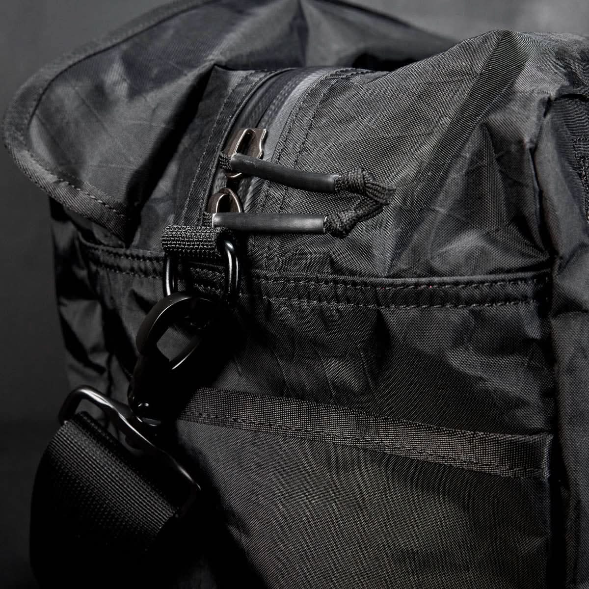 Close-up of the Kit Bag - X-PAC in black, crafted from X-PAC VX21 nylon with a zipper, strap, and metal clasp, set against a dark background.