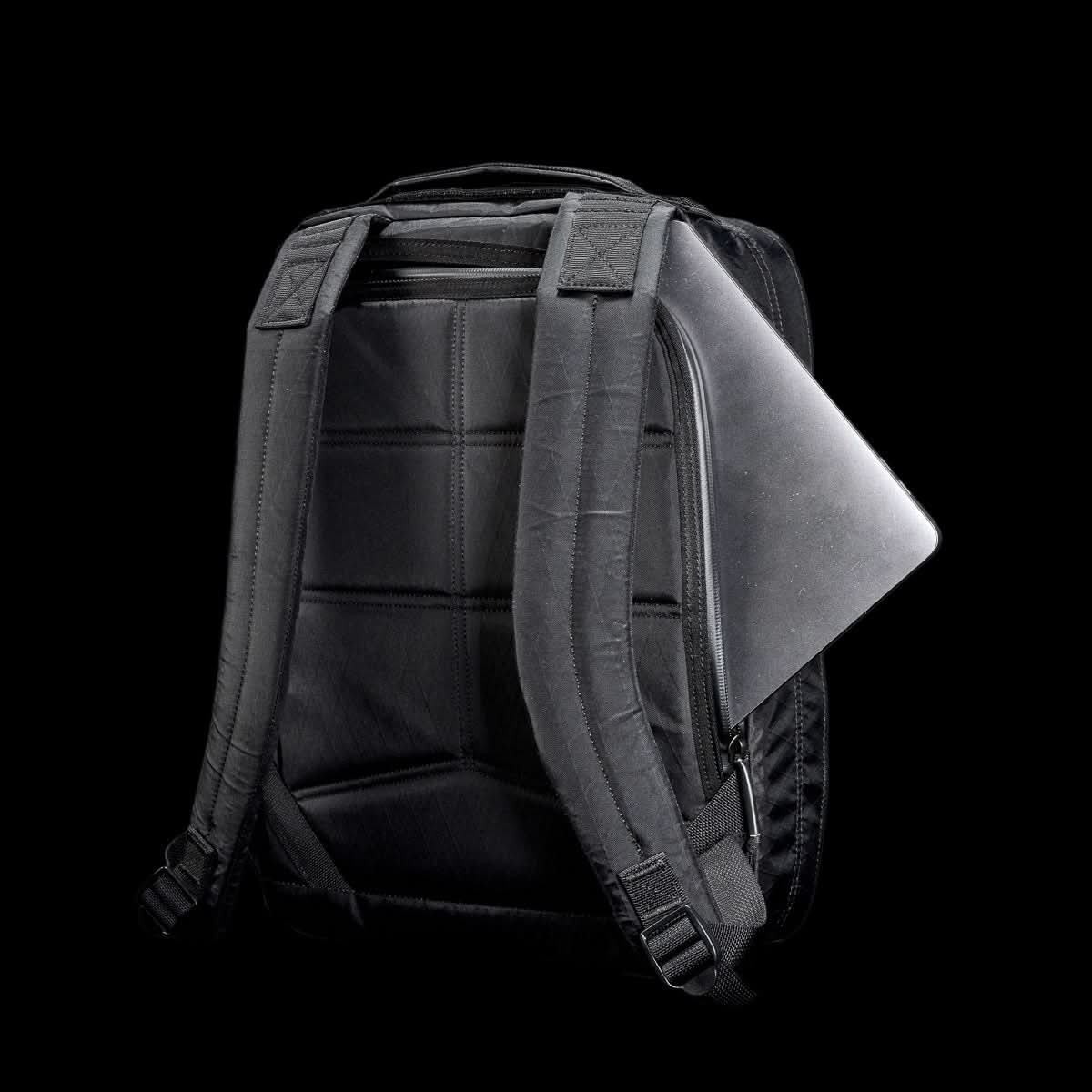 The GR0 - X-PAC is a black, lightweight rucksack with padded straps and waterproof material, featuring a gray laptop partially visible in the back compartment.