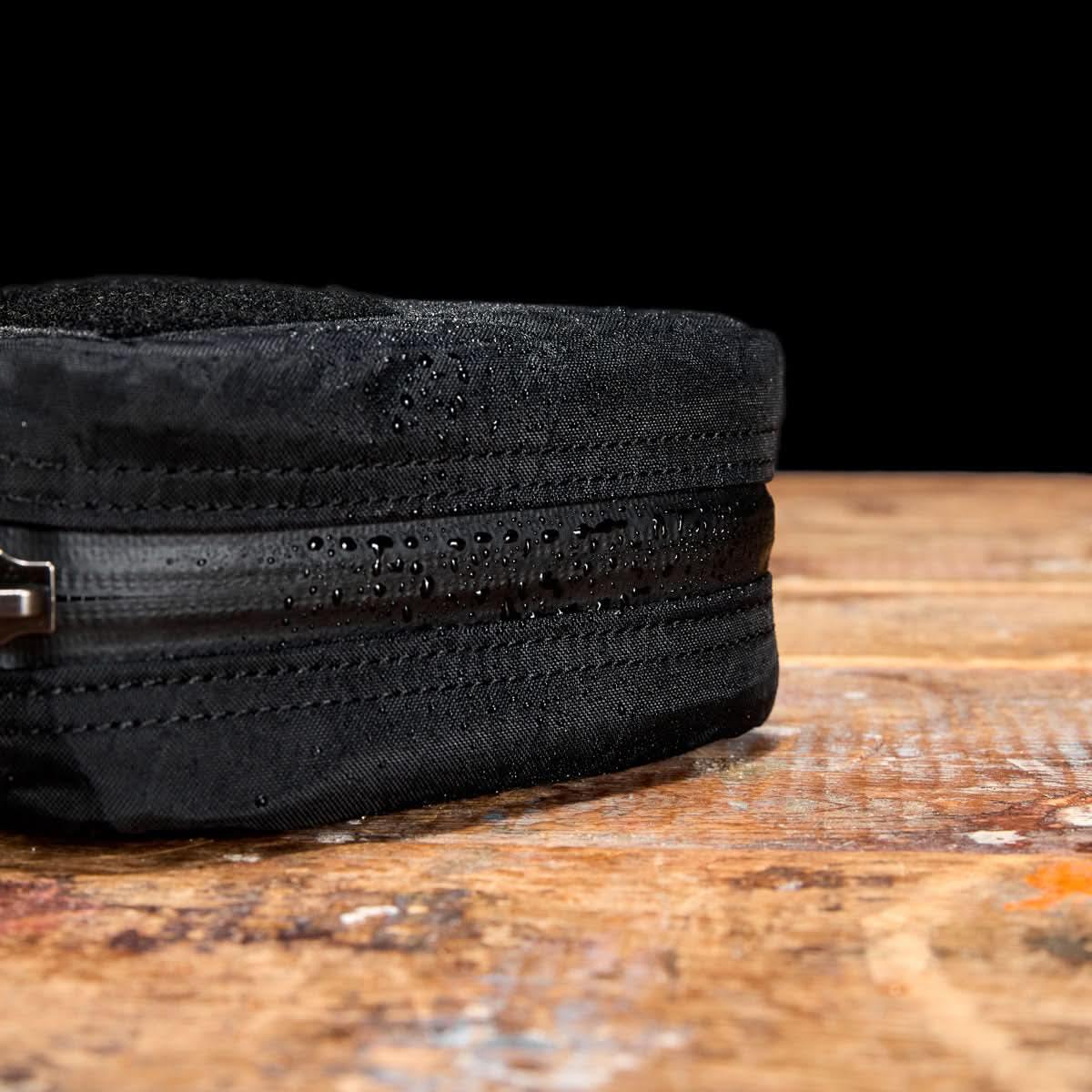 Close-up of black waterproof GORUCK gear bag with water droplets on zipper and fabric on wooden surface