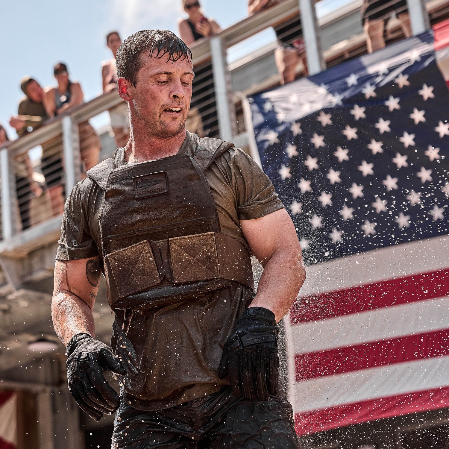 A man in wet tactical gear stands in front of a U.S. flag with water splashing around him, demonstrating the durability and comfort of our Slick Short Sleeve Tee - Tri-BlendX.