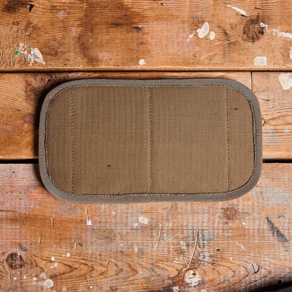 Close-up of a rectangular coyote brown Cordura fabric panel on worn wooden surface, featuring detailed stitching