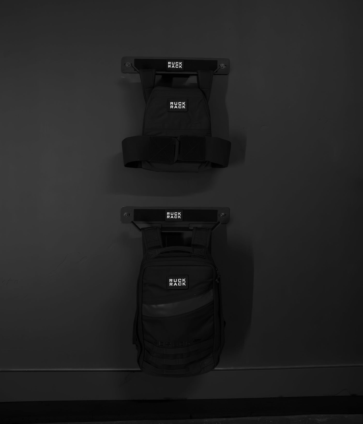 Two black backpacks labeled “Ruck Pack” hang on a sleek, dark grey Ruck Rack® Delta—an ideal heavy-duty wall mount storage solution for rucks, weight vests, and tactical gear.