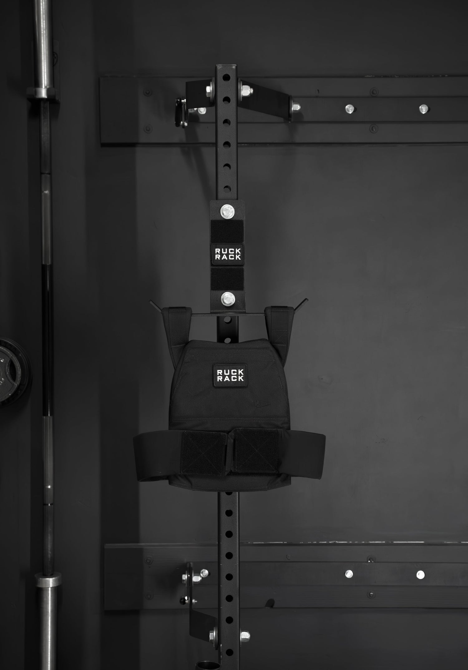 A Ruck Rack® Monster, a versatile mount for rucks, weight vests, and tactical gear, is mounted on a metal storage rack in the gym alongside a barbell—showcasing a sturdy organizer ideal for American-made gear storage.