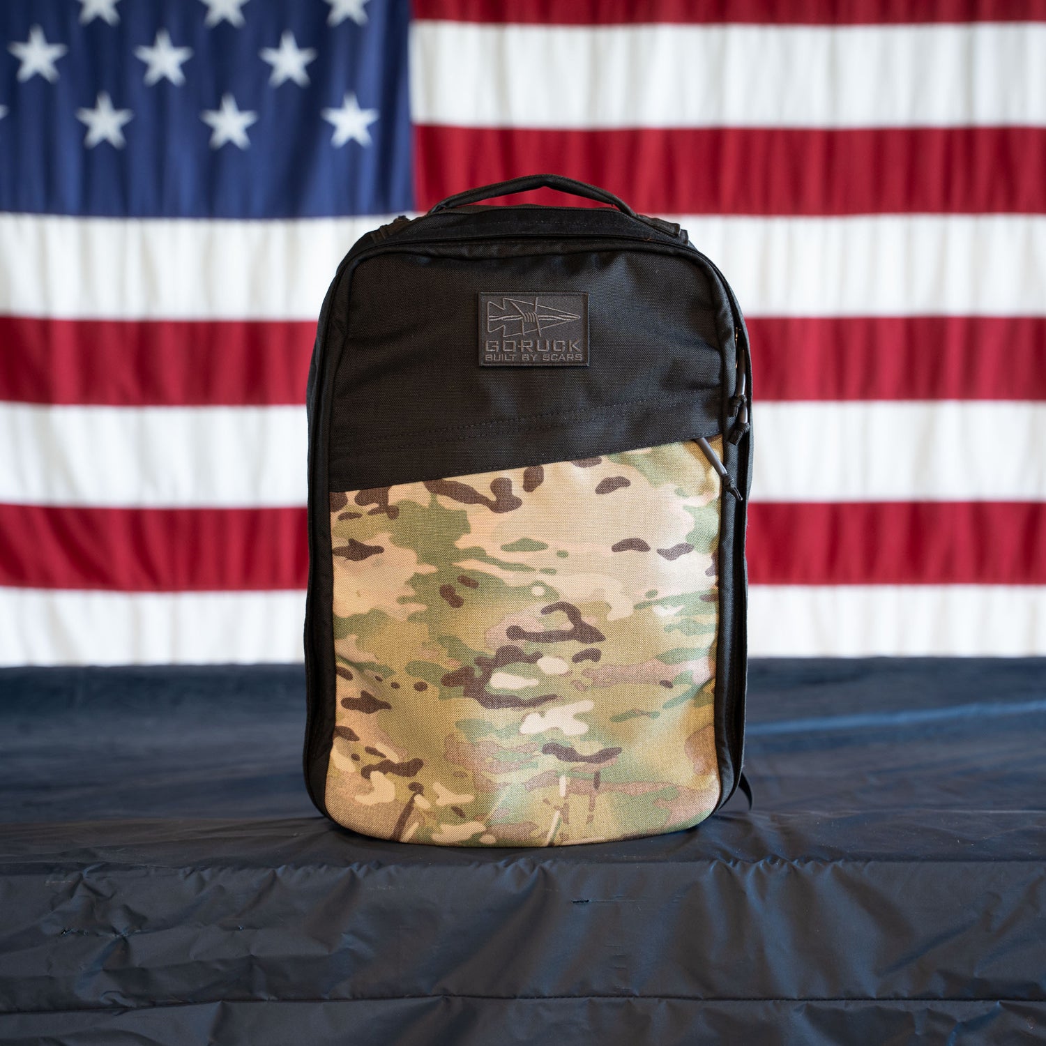 A GR1 Shooter - Built by Scars backpack with a black top is displayed before an American flag backdrop, ready for any SCARS mission.
