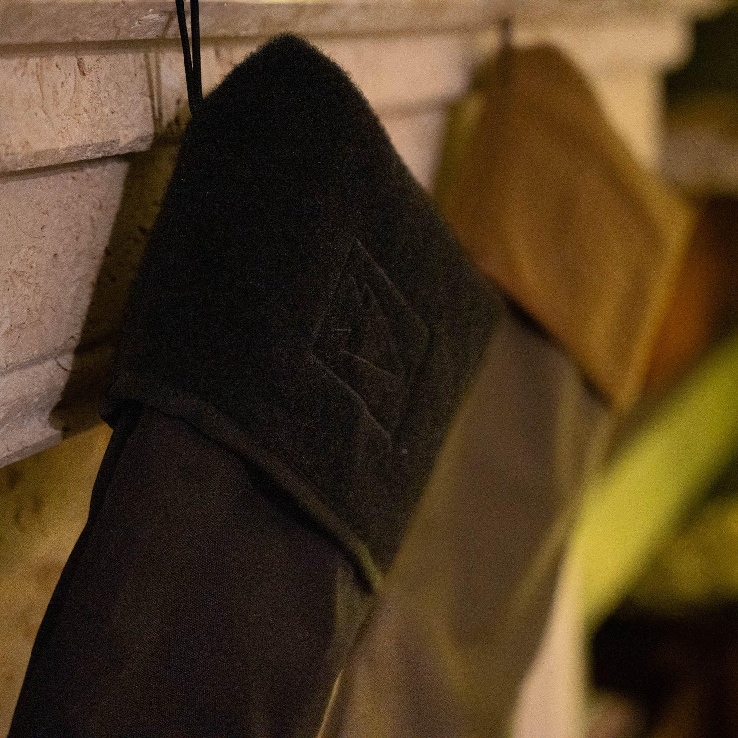 Close-up of a black GORUCK stocking with embroidered logo hanging near a fireplace