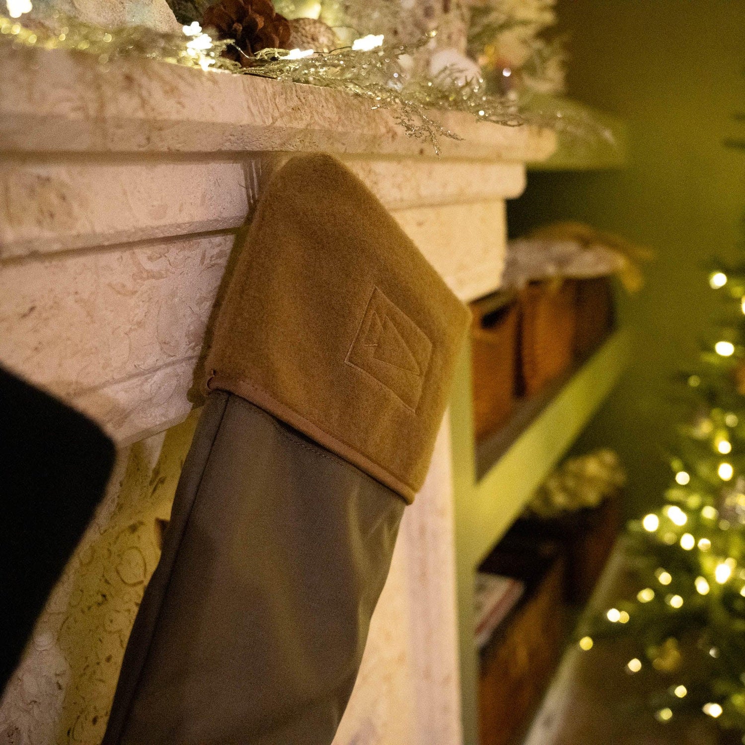GORUCK branded brown and gray stocking hanging on a decorated fireplace mantel with warm holiday lights in background