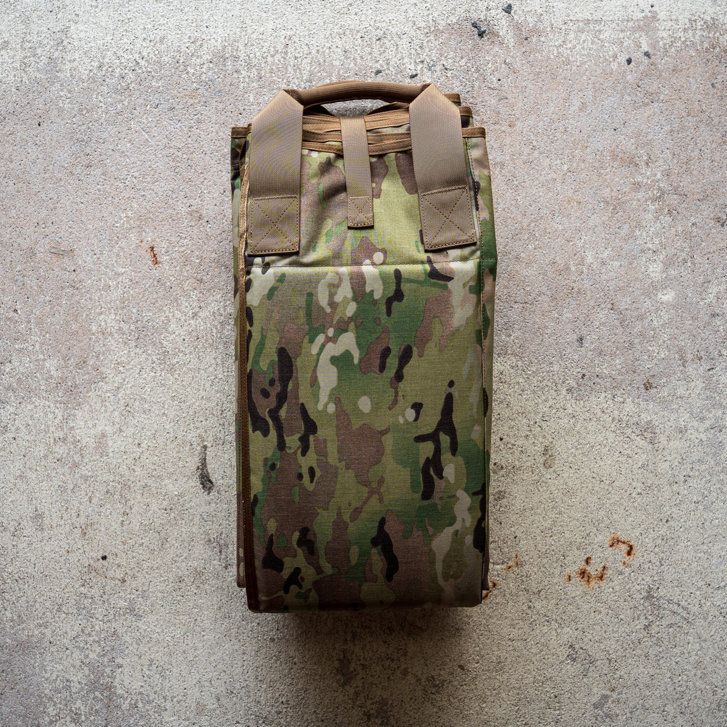 A folded camouflage-patterned Shooting Mat rests on a textured concrete surface.