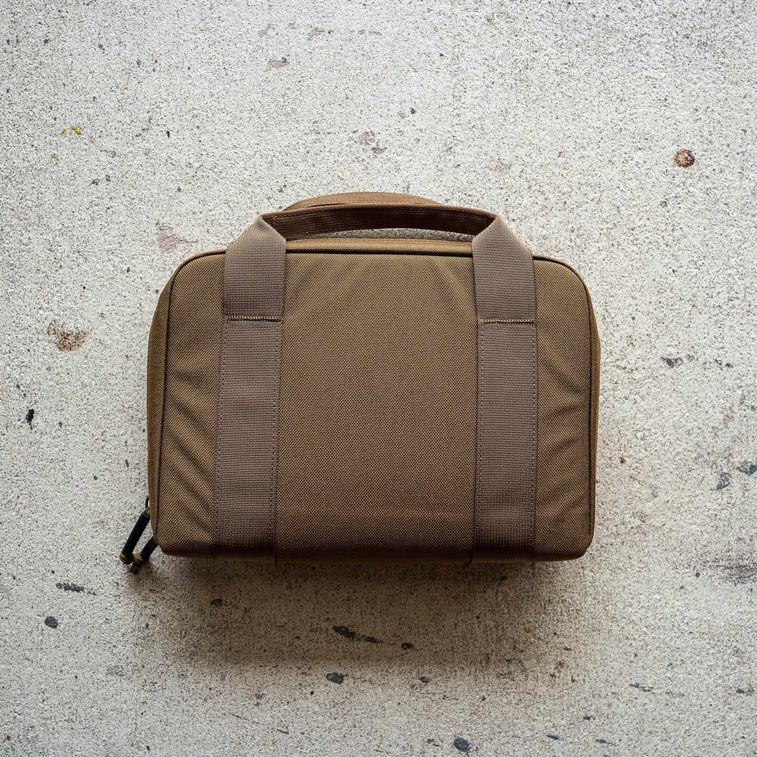 The Pistol Rug, a brown soft-sided modular pistol case with two handles, rests on a light textured concrete surface.