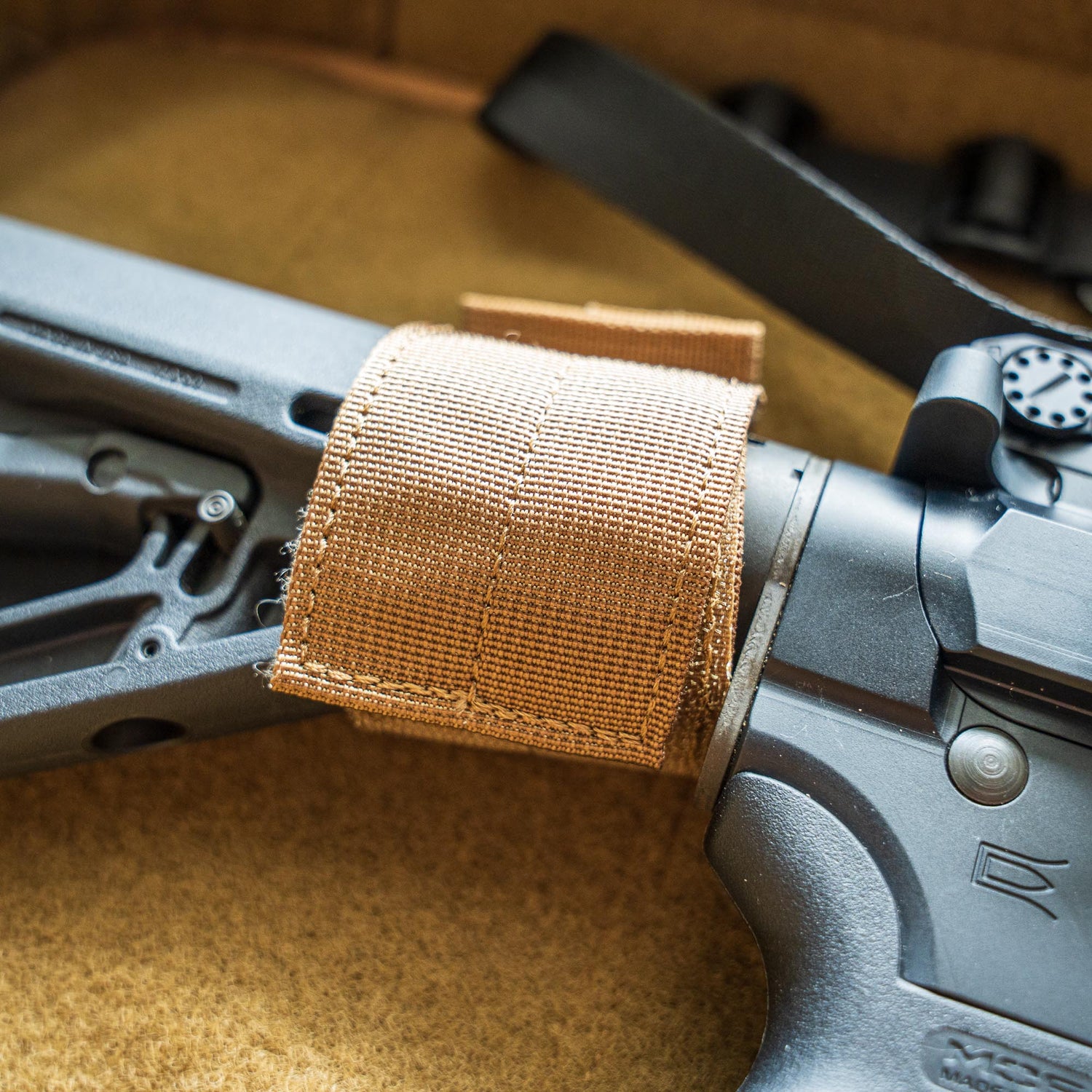 Close-up of the Retention Package's tan nylon strap securing a black firearm stock on a tan surface.