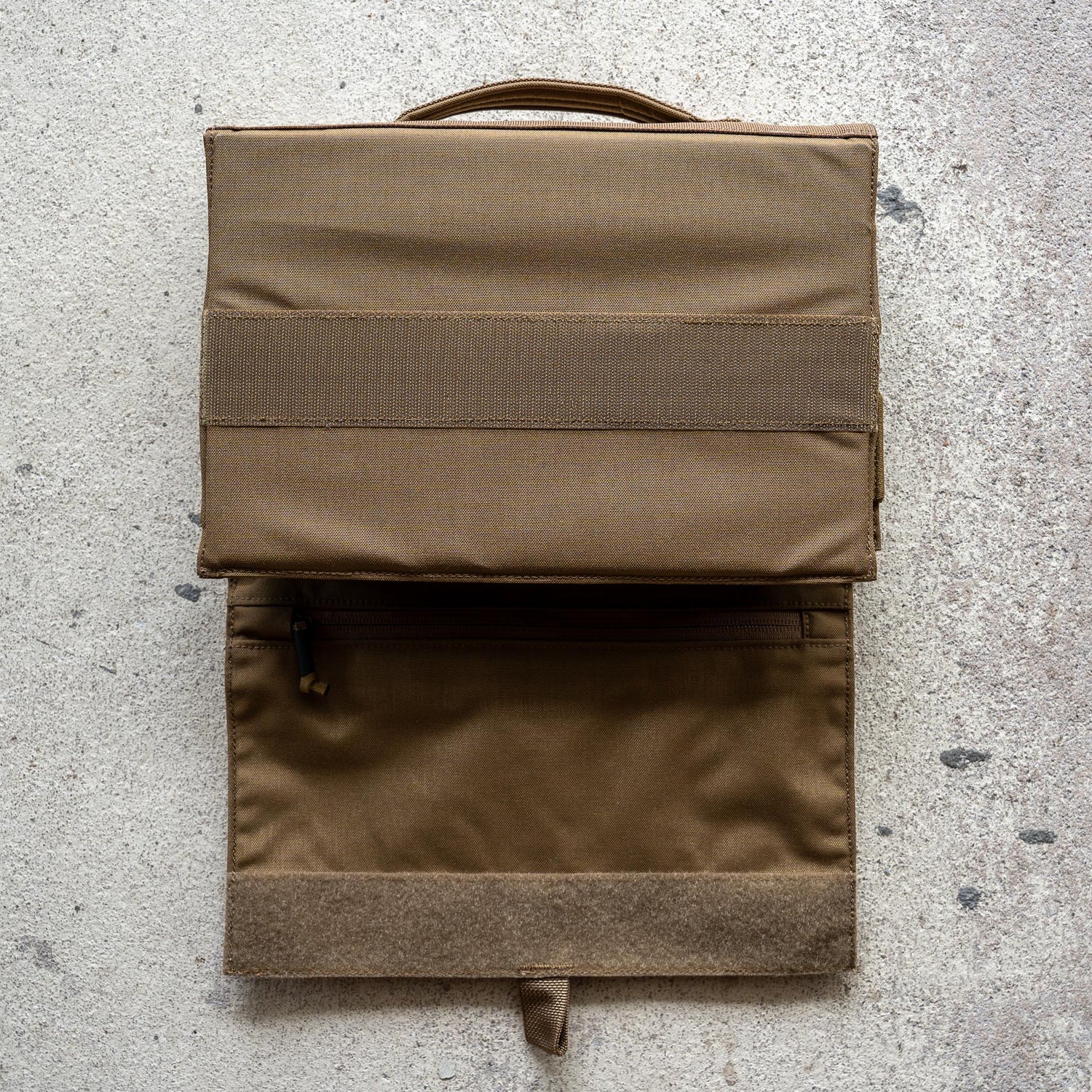 The Ammo Book is a brown fabric bullet organizer pouch with a handle and zippered pocket, shown open on a textured surface.