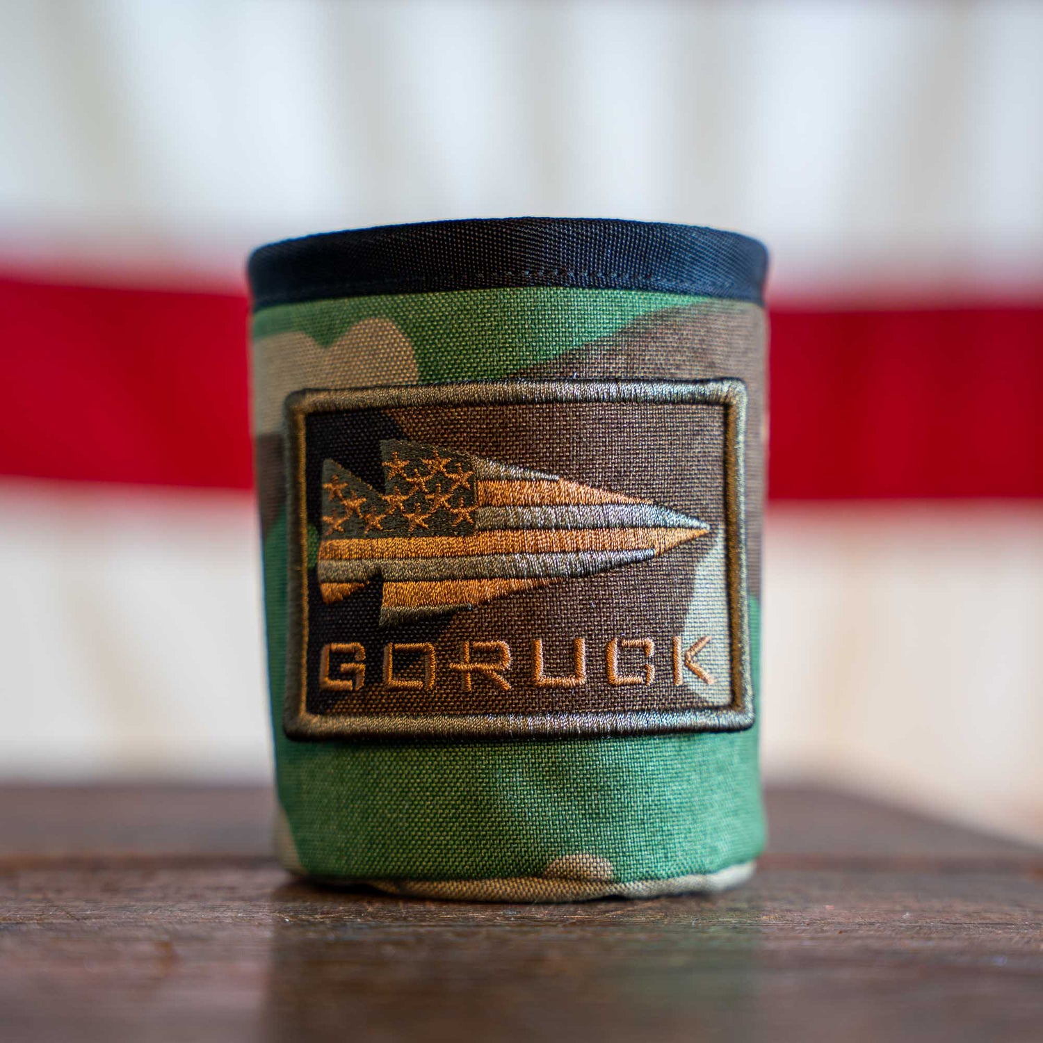 The Ballistic Beer Jacket is a camo GORUCK beer koozie featuring a patch with a stylized American flag arrowhead.