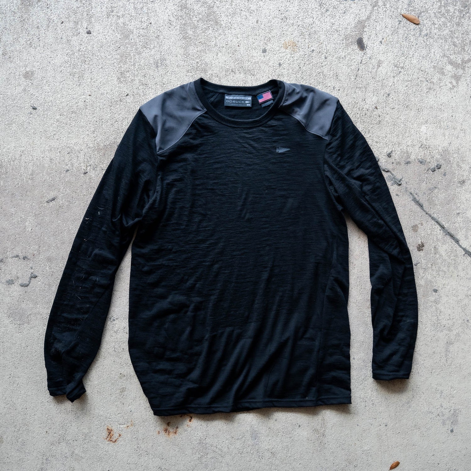 Men’s Commando Long Sleeve - Merino Wool in black, featuring reinforced shoulders and a classic commando sweater design, laid flat on a concrete surface.