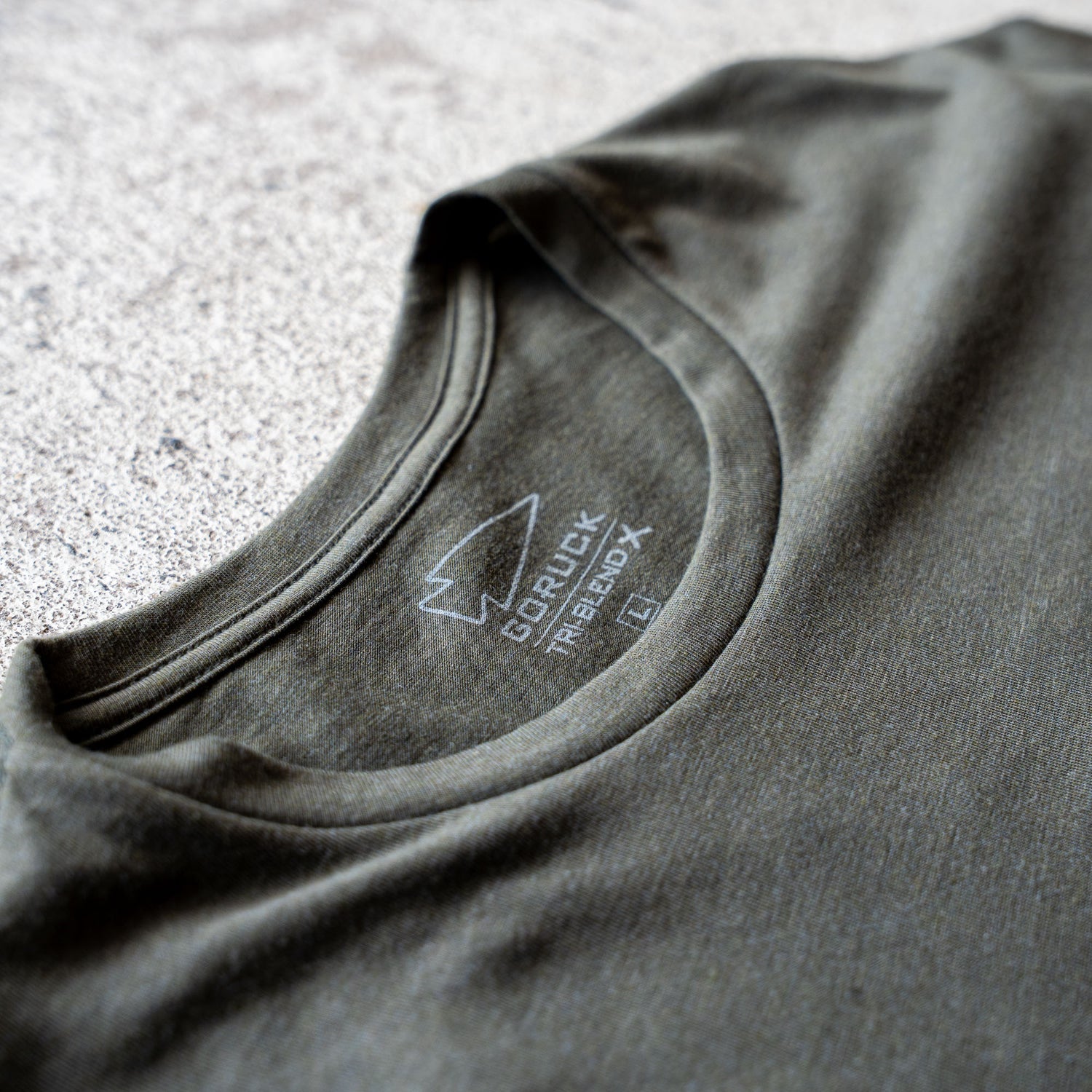 Close-up of a green collar from the Slick Short Sleeve Tee - Tri-BlendX, featuring a printed GORUCK logo and size label on the inside, highlighting the shirt's durable and comfortable premium Tri-BlendX fabric.
