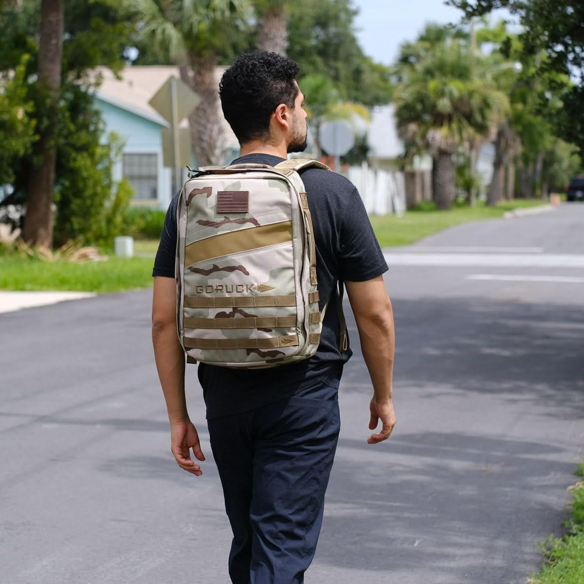 Man walking on a suburban street wearing a camo GORUCK backpack with tactical design
