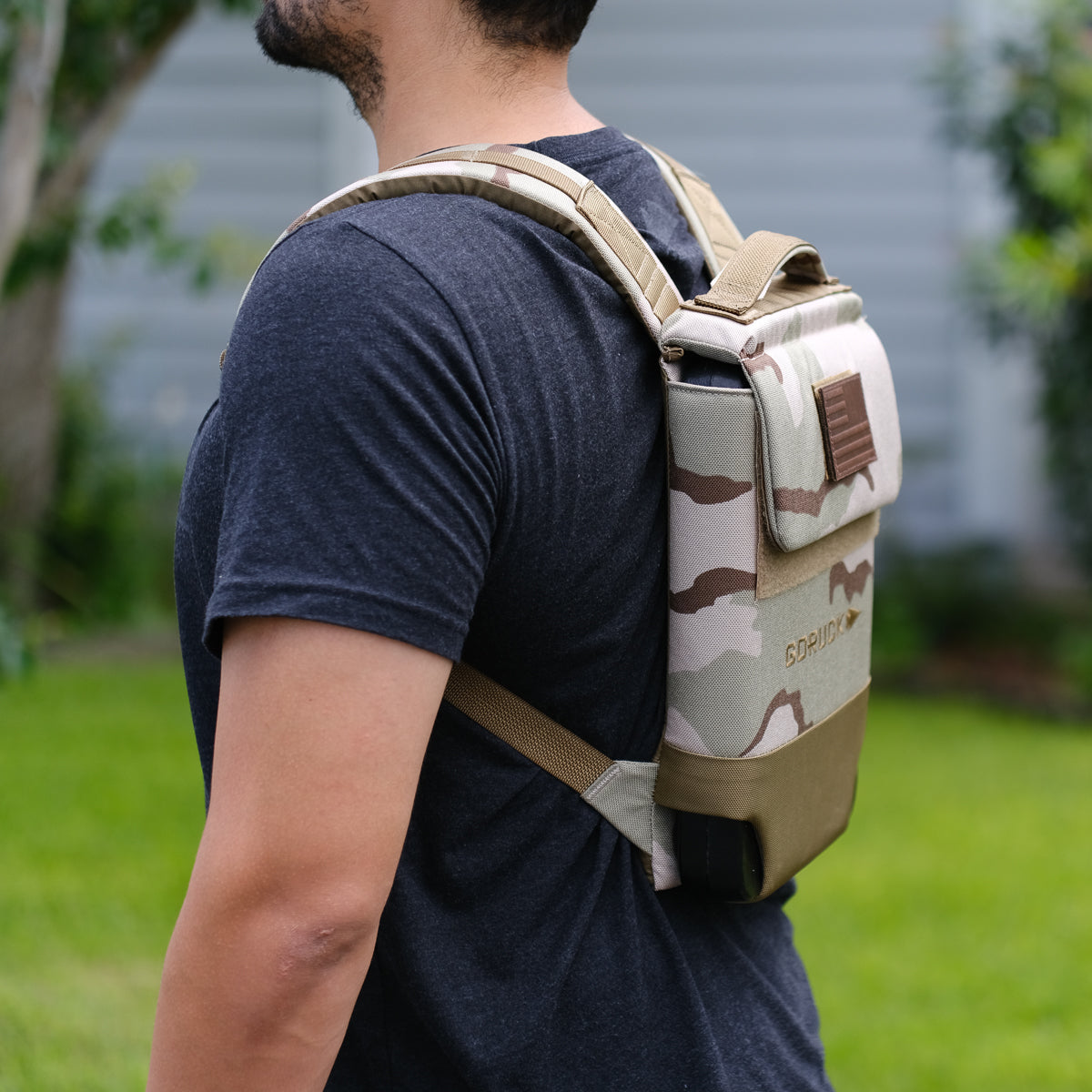 Man wearing a Ruck Plate Carrier 3.0 with padded shoulder straps, standing sideways outdoors in a grassy yard.