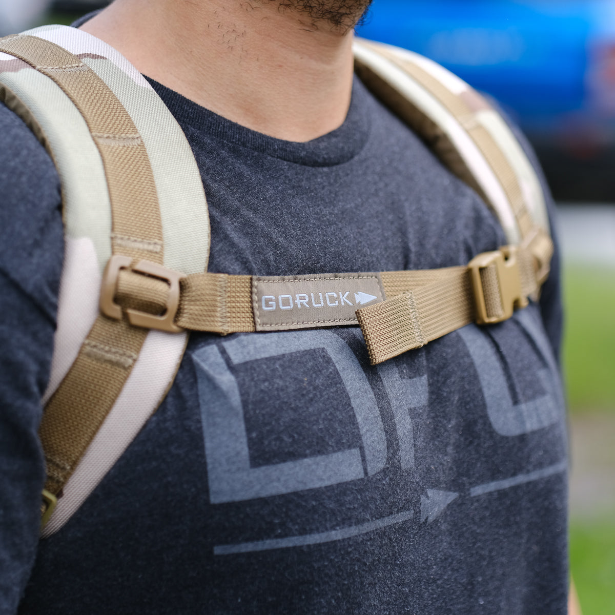 Close-up of a person wearing a black shirt and the Ruck Plate Carrier 3.0 in tan, with a visible chest strap, highlighting its durable ballistic nylon construction.