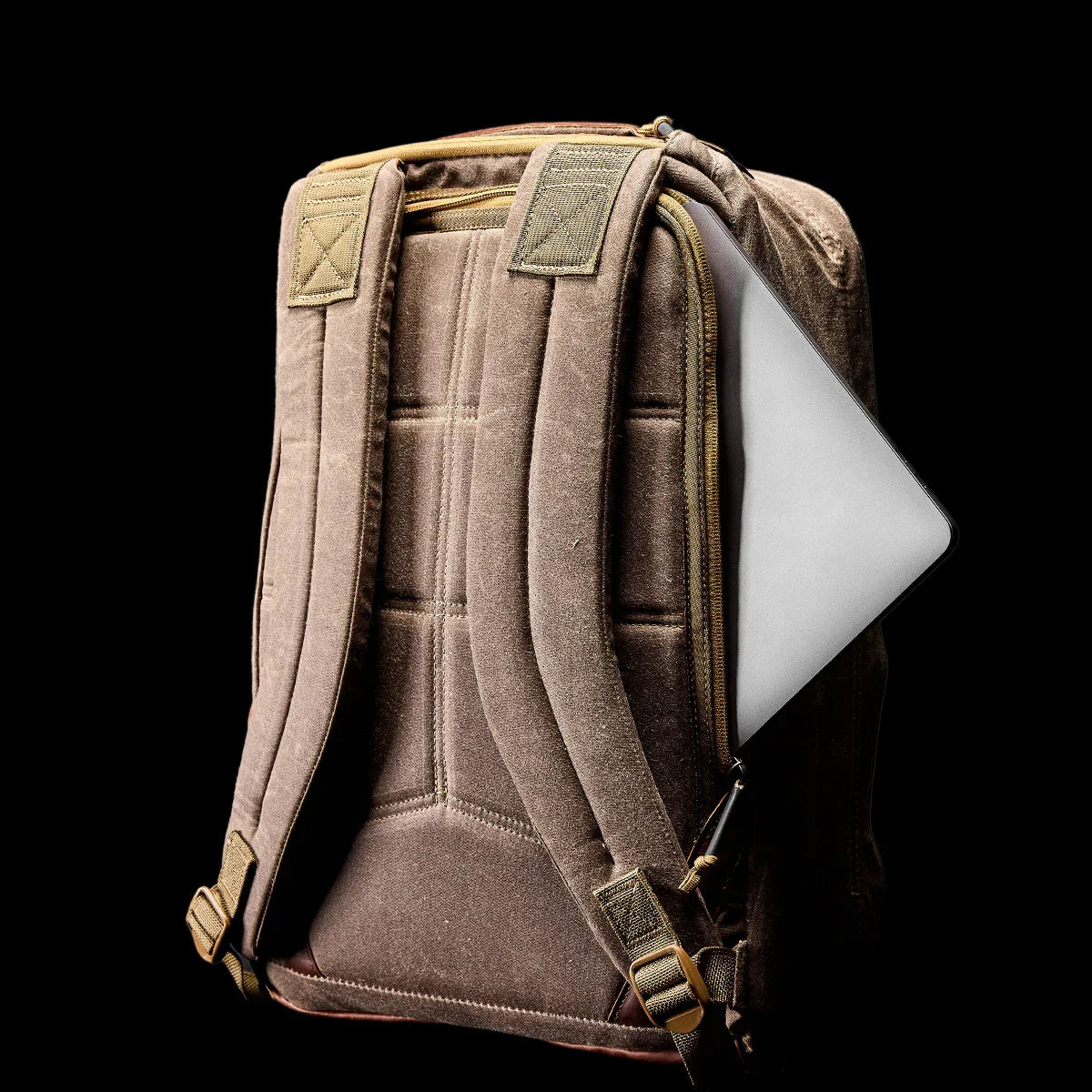 Dark Oak GORUCK backpack with padded straps and laptop partially inside side zipper pocket on black background