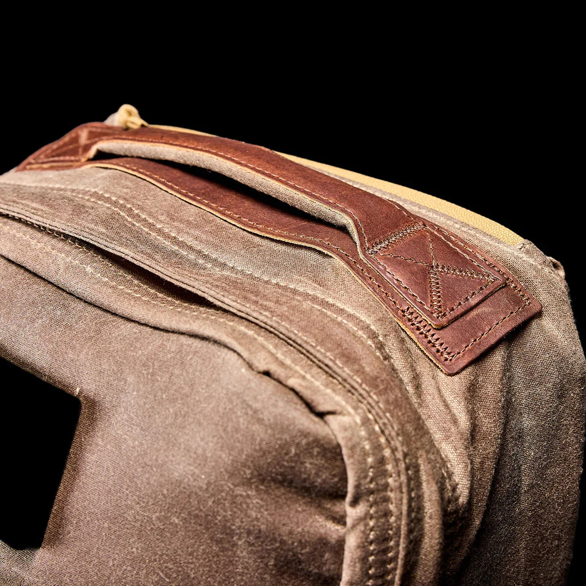 Close-up of durable dark oak fabric rucksack handle with brown leather grip and reinforced stitching on black background