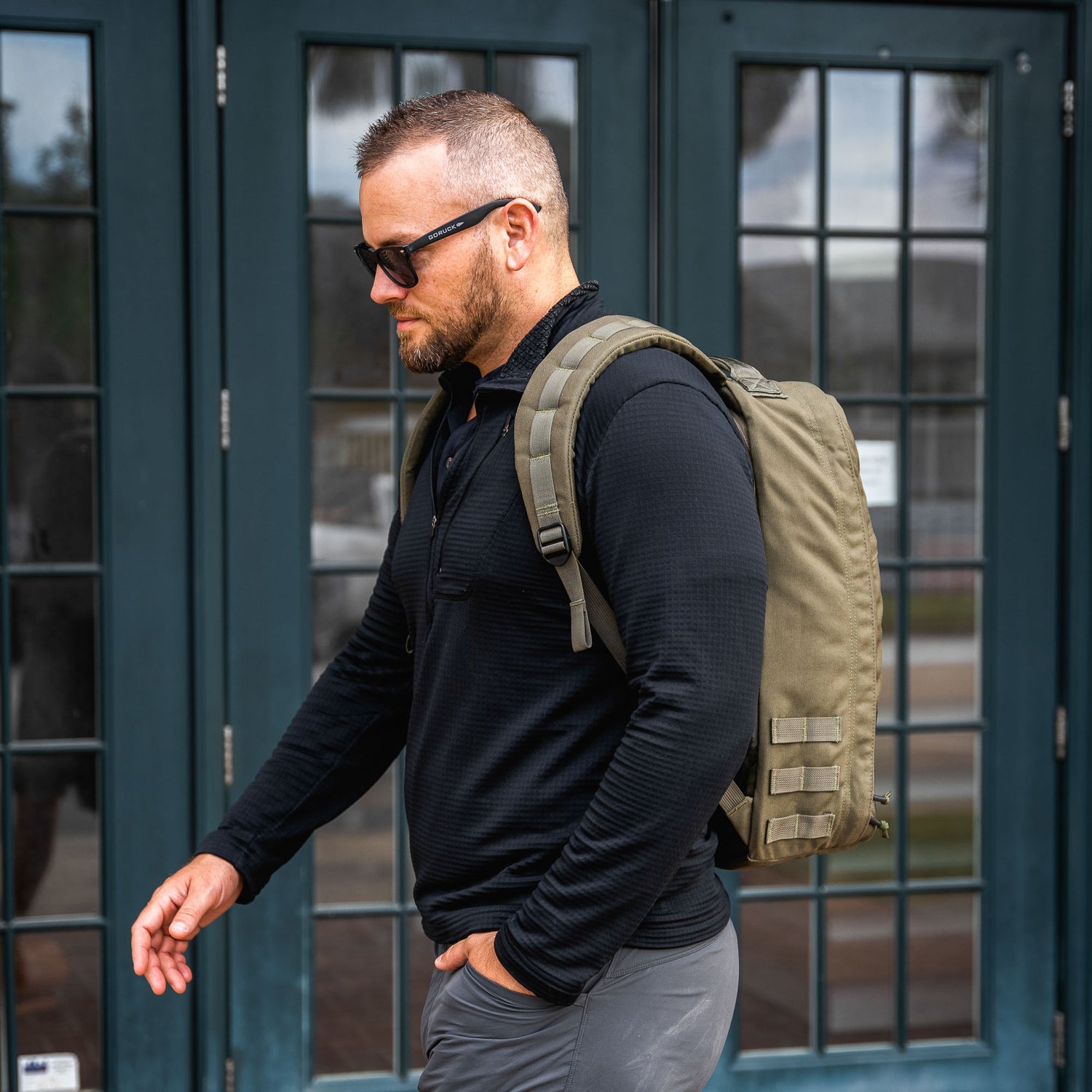 A man wearing sunglasses carries his essentials in style with the GR1 USA - Cordura rucksack, renowned for its Special Forces grade durability.