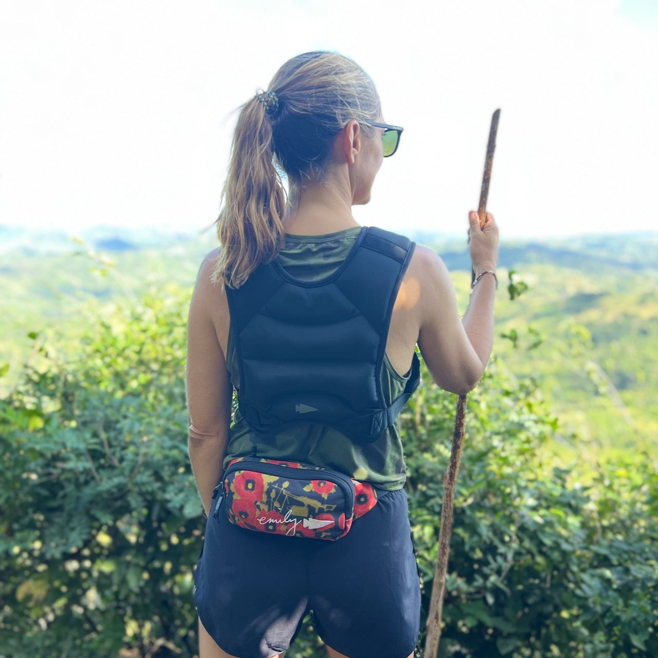 A woman hikes with a stick, overlooking a green landscape while wearing the Spy Ruck Women's Weighted Vest.