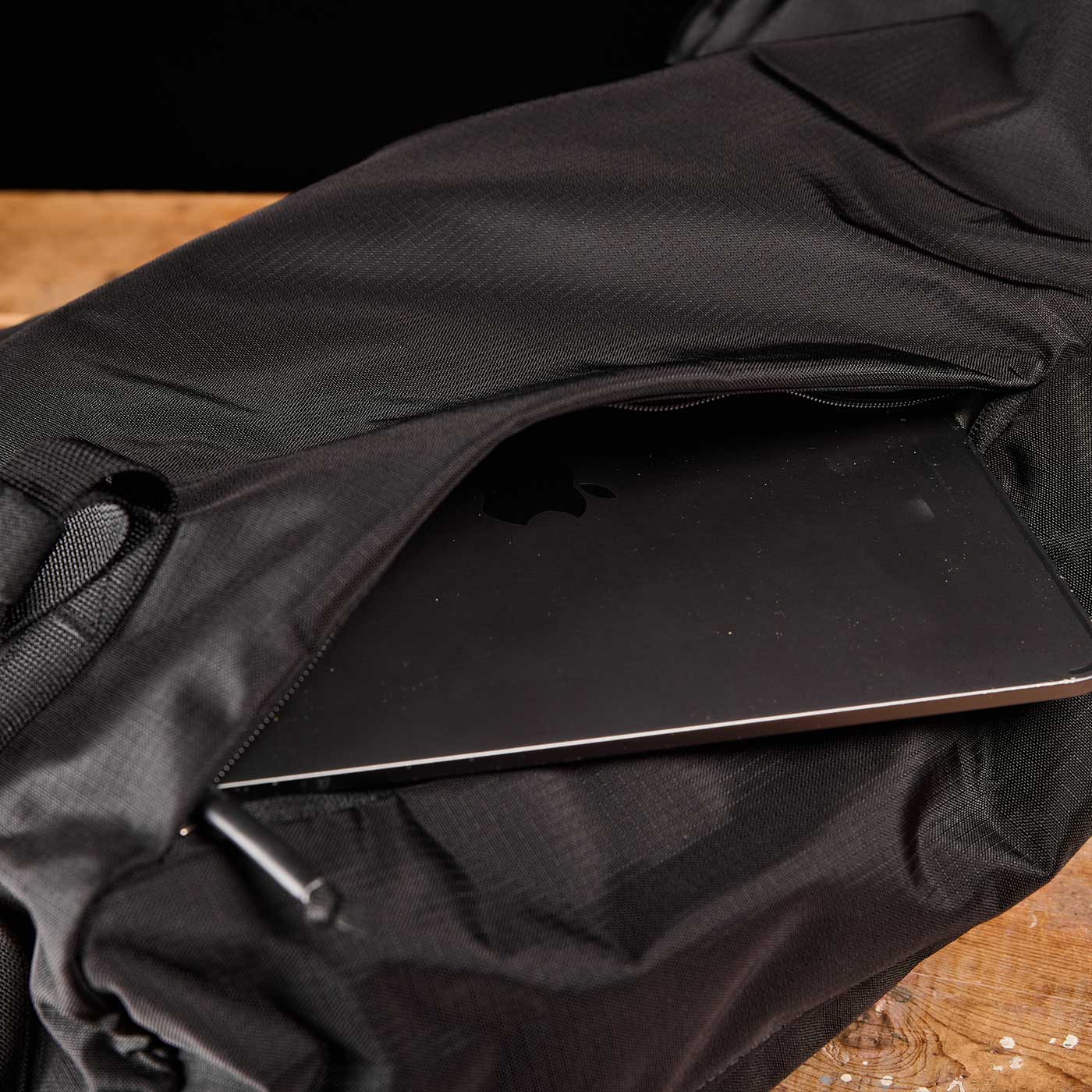 A black laptop partially tucked into the zippered pocket of a black bag on a wooden surface.