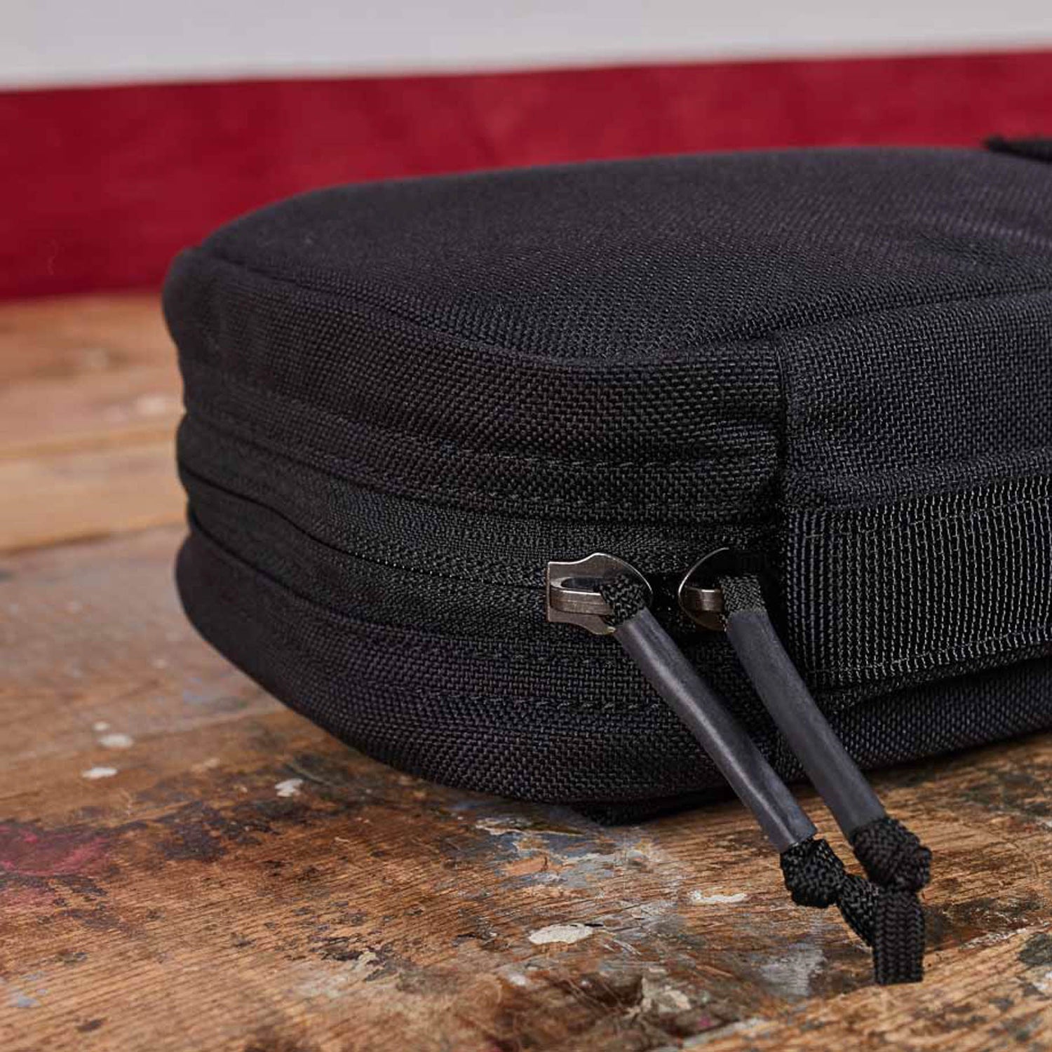 Close-up of the GR1 Field Pocket - USA, a black zippered pouch with dual zipper pulls, perfect as an electronics organizer, shown resting on a wooden surface.