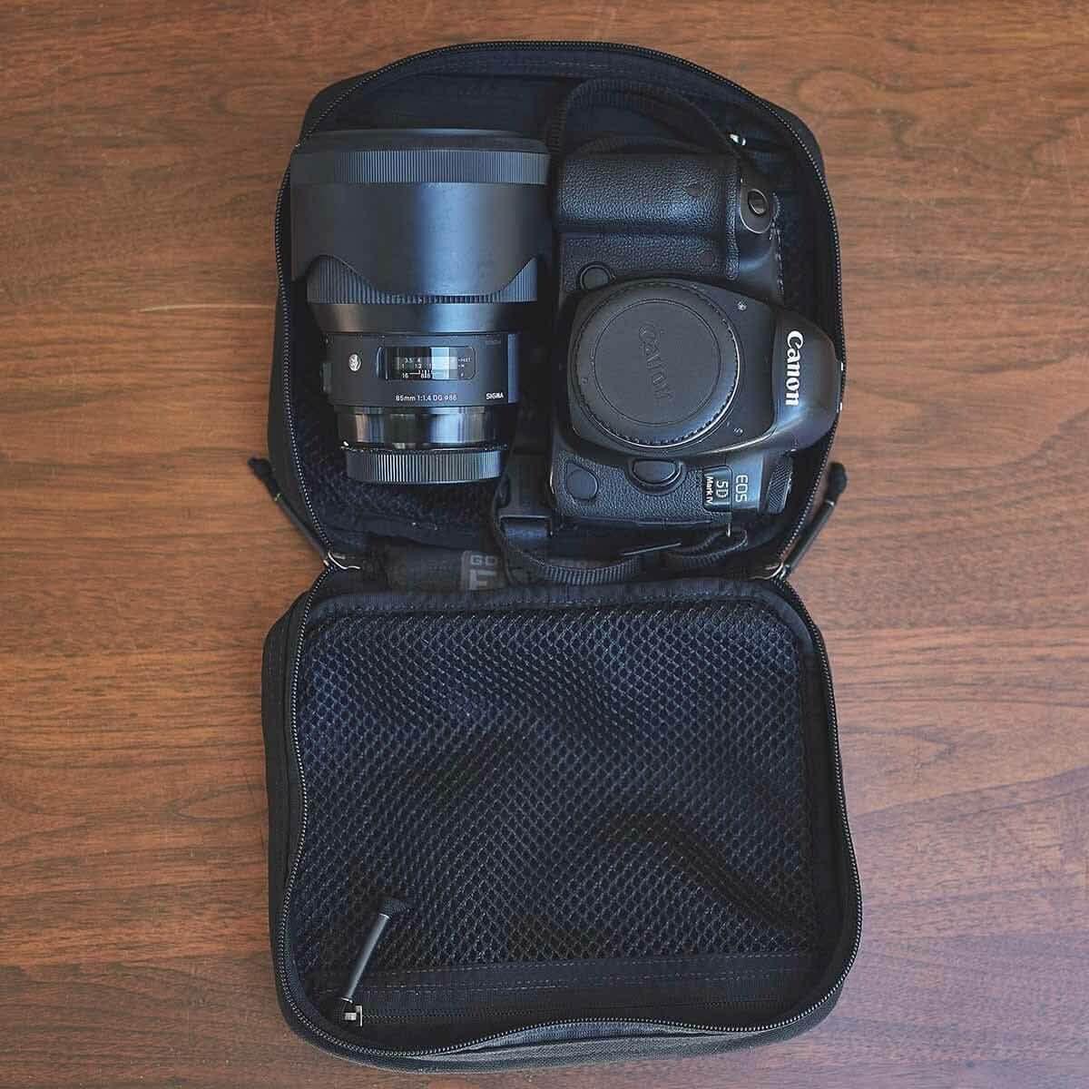 Compact black camera case with Canon EOS 5D Mark IV and Sigma 85mm lens on wooden surface