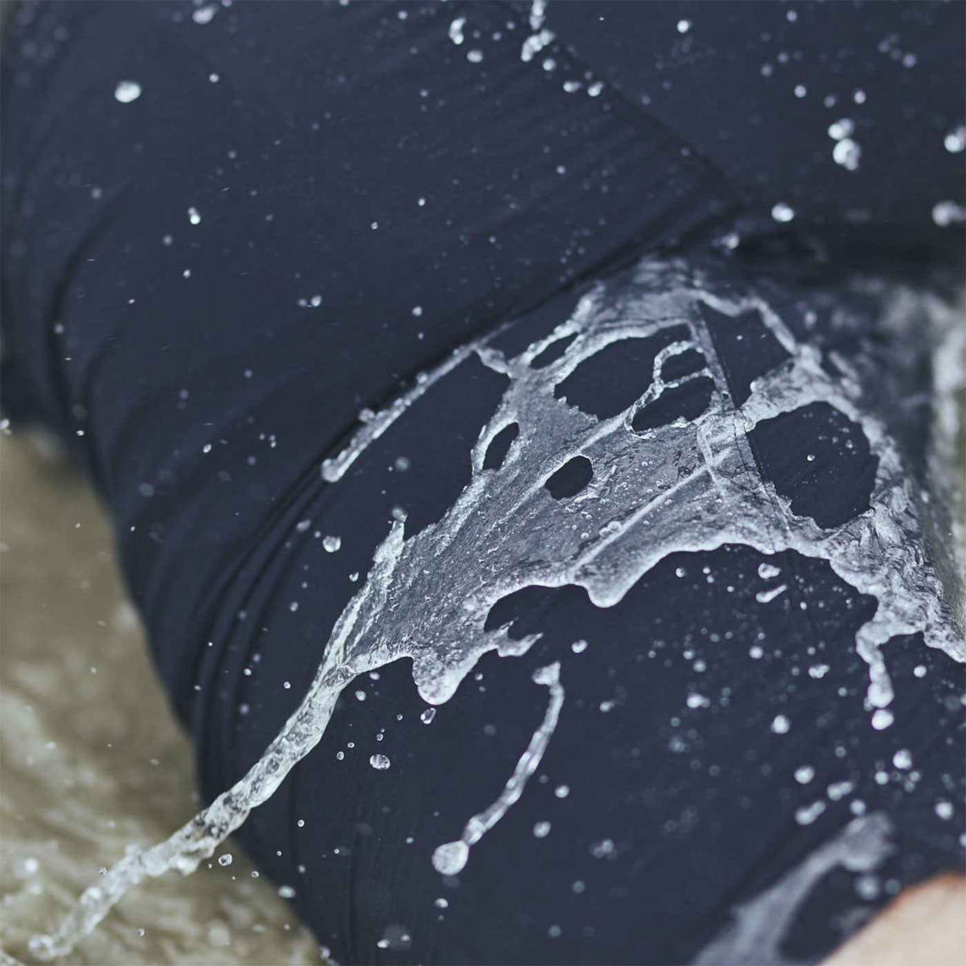 Close-up of water splashing on dark fabric, likely swimwear, with blurred water in the background.