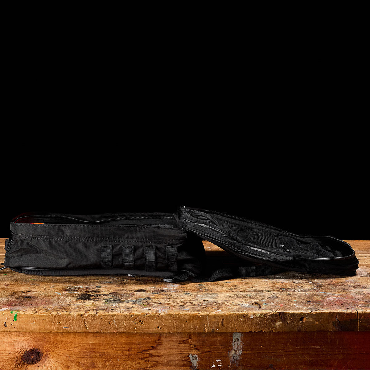 A black, partially unzipped bag lies flat on a worn wooden table against a black background.