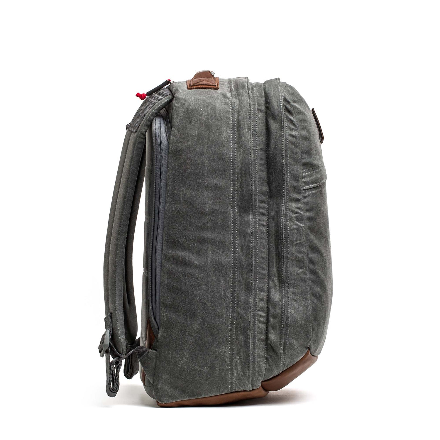Side view of the GR2 - Heritage Waxed Canvas backpack in green with brown Red Wing Leather accents and padded shoulder straps, standing upright.
