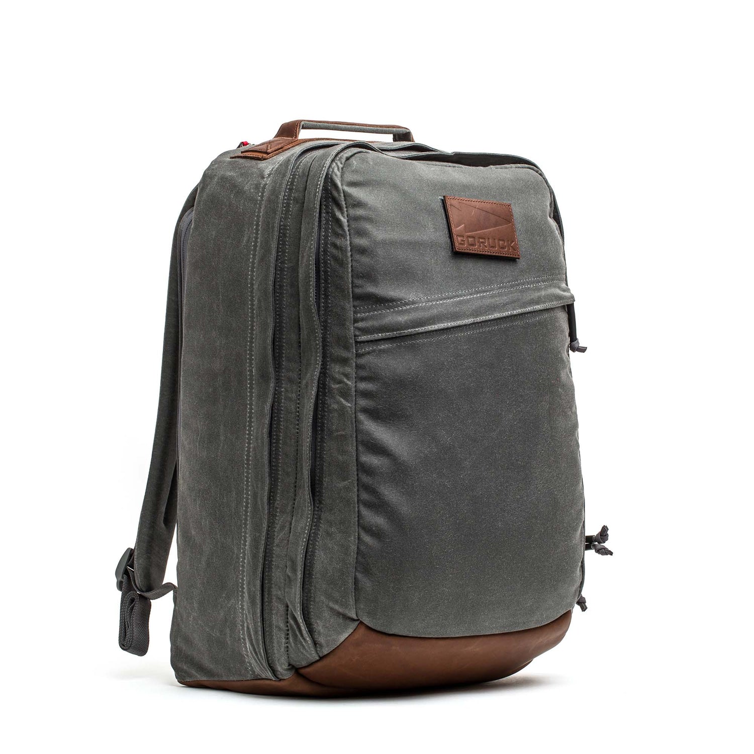 The GR2 - Heritage Waxed Canvas backpack features gray waxed canvas, brown Red Wing Leather accents, a front zipper pocket, and top handle. Stylish and practical, this travel ruck stands upright on a white background.
