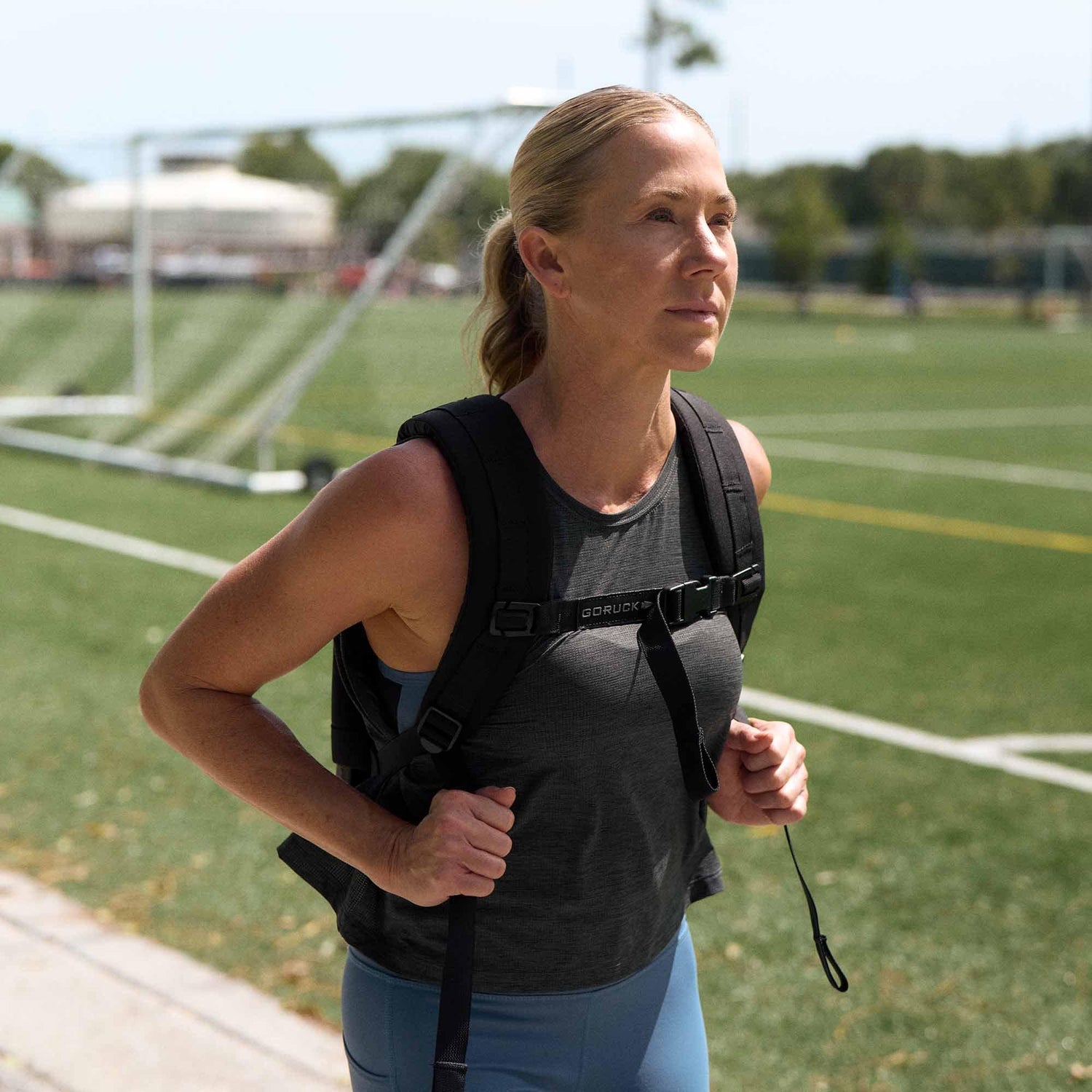 Woman rucking with GORUCK backpack on sports field, showcasing durable fitness gear