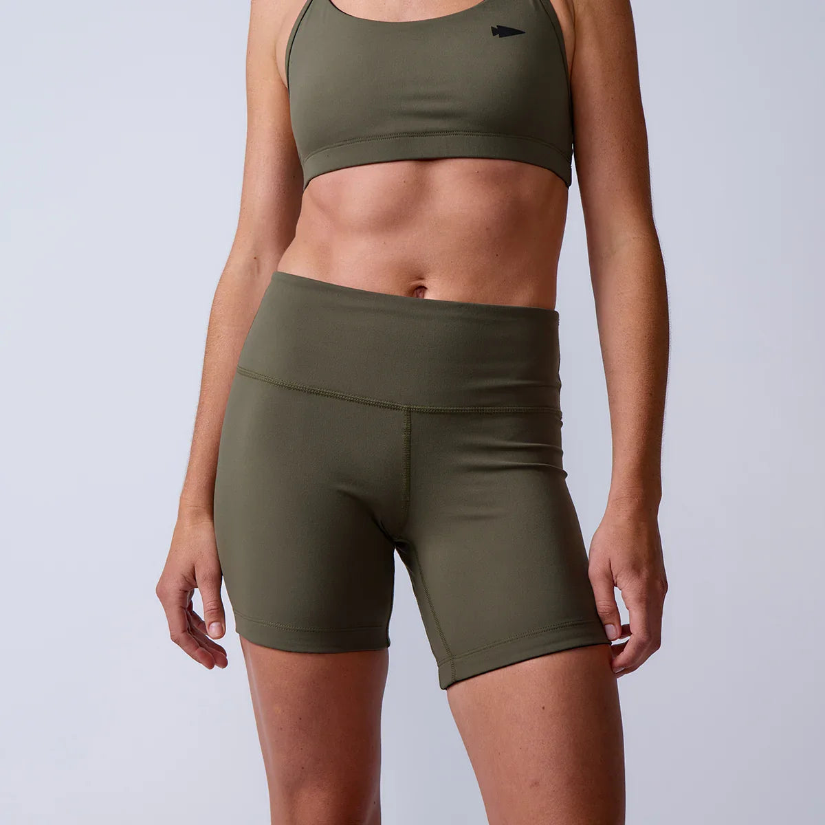 Close-up of woman wearing olive green athletic high-waisted shorts and sports bra with minimalist logo