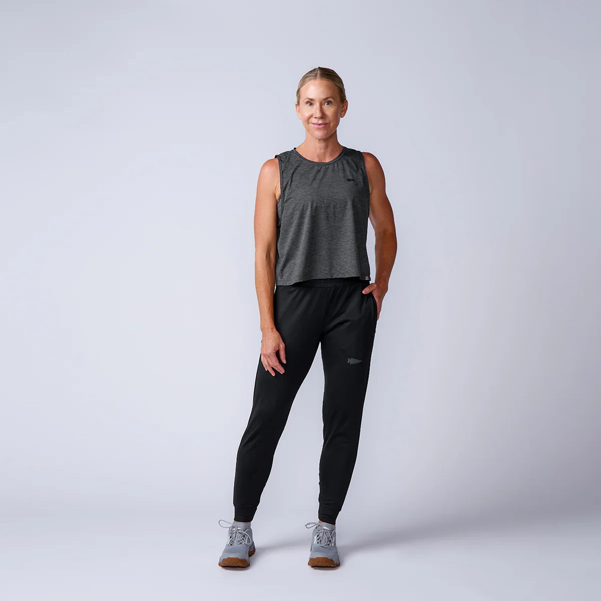 fit woman in black sleeveless rucking top and black jogger pants with gray sneakers on studio background