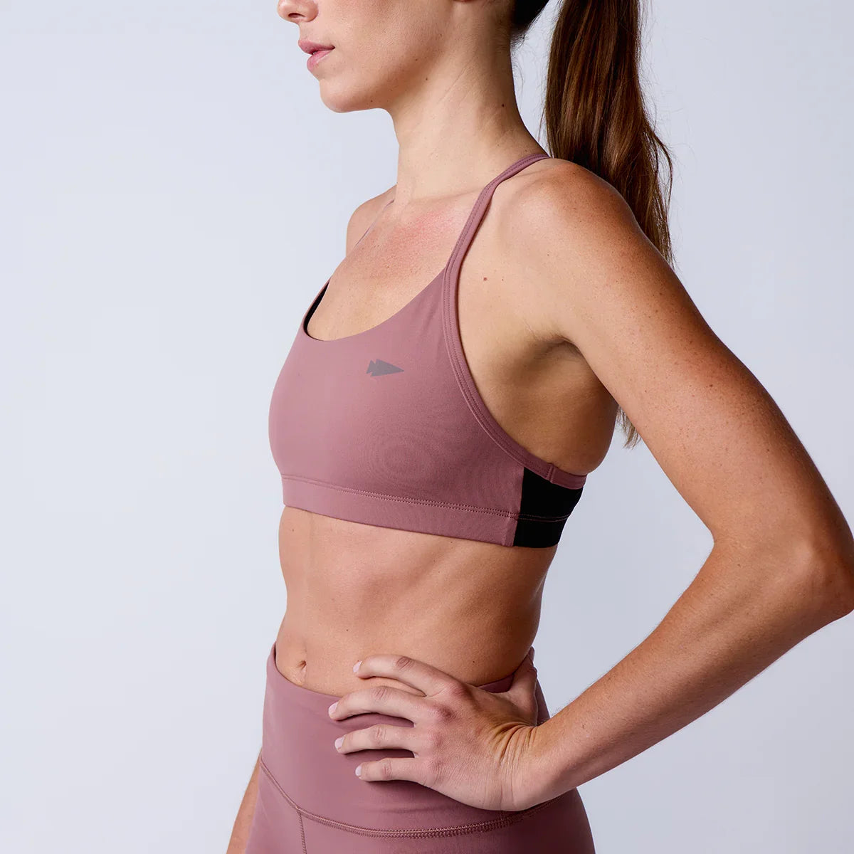Close-up side view of woman wearing mauve GORUCK sports bra and leggings against plain background