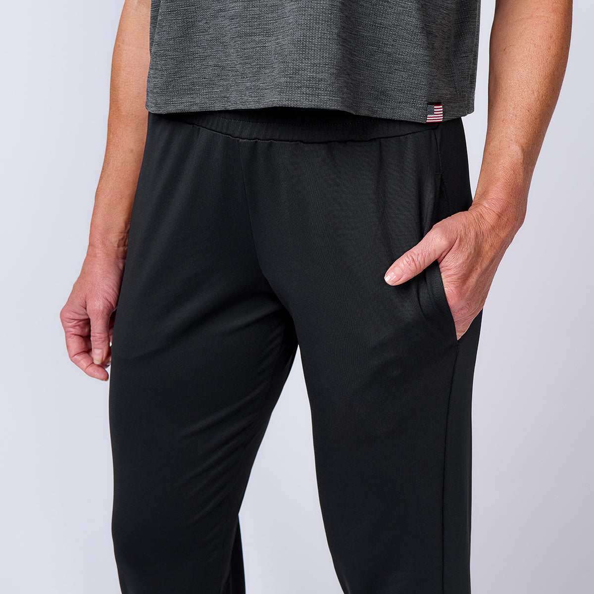 A person is shown from the shoulders down wearing a gray shirt and the Women’s Training Performance Joggers in black, with one hand in their pocket.