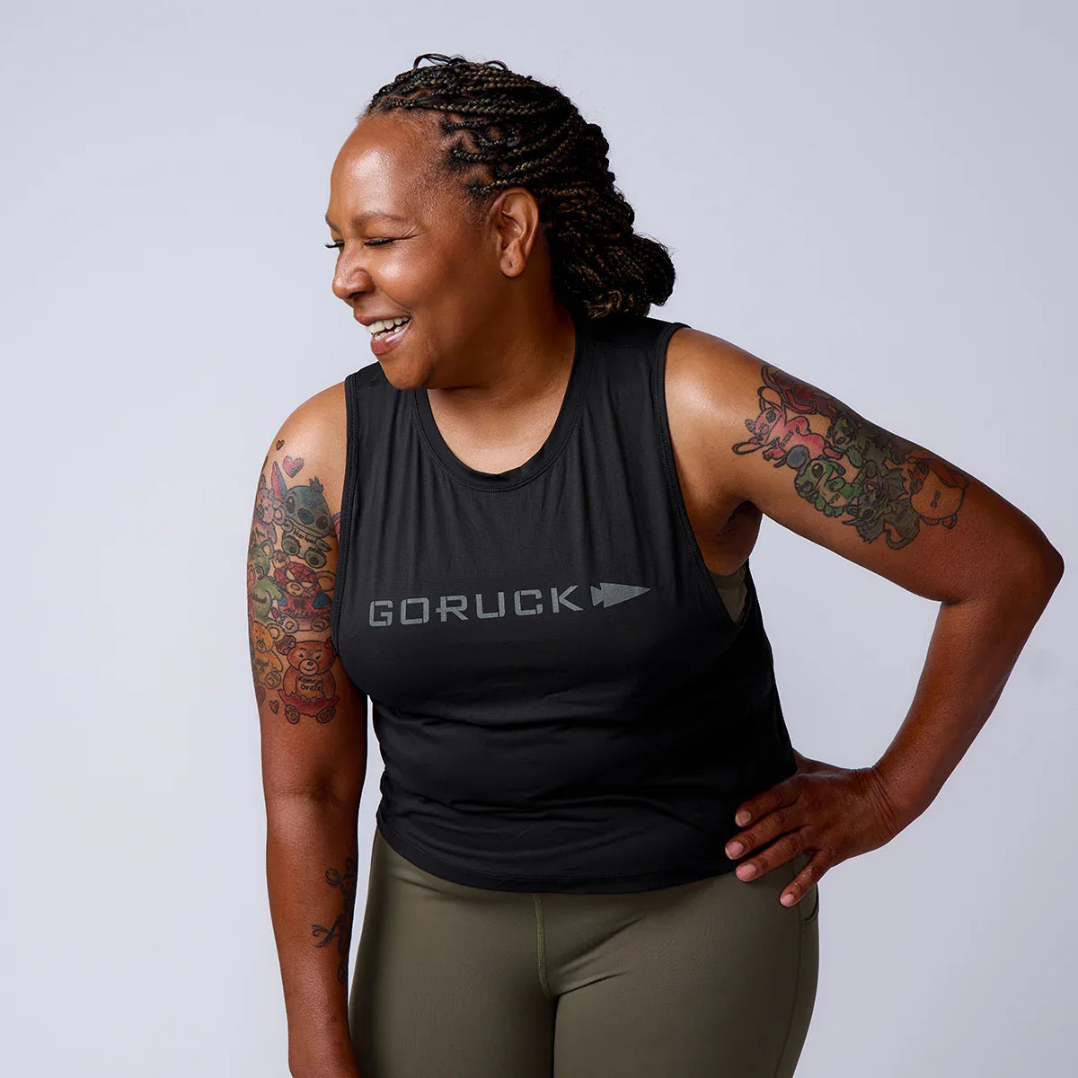 Smiling woman in GORUCK tank top with tattooed arms, showcasing rucking fitness gear