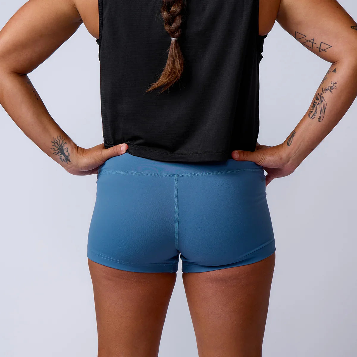 Rear view of person with braided hair wearing black sleeveless top, blue athletic shorts, and tattoos on arms