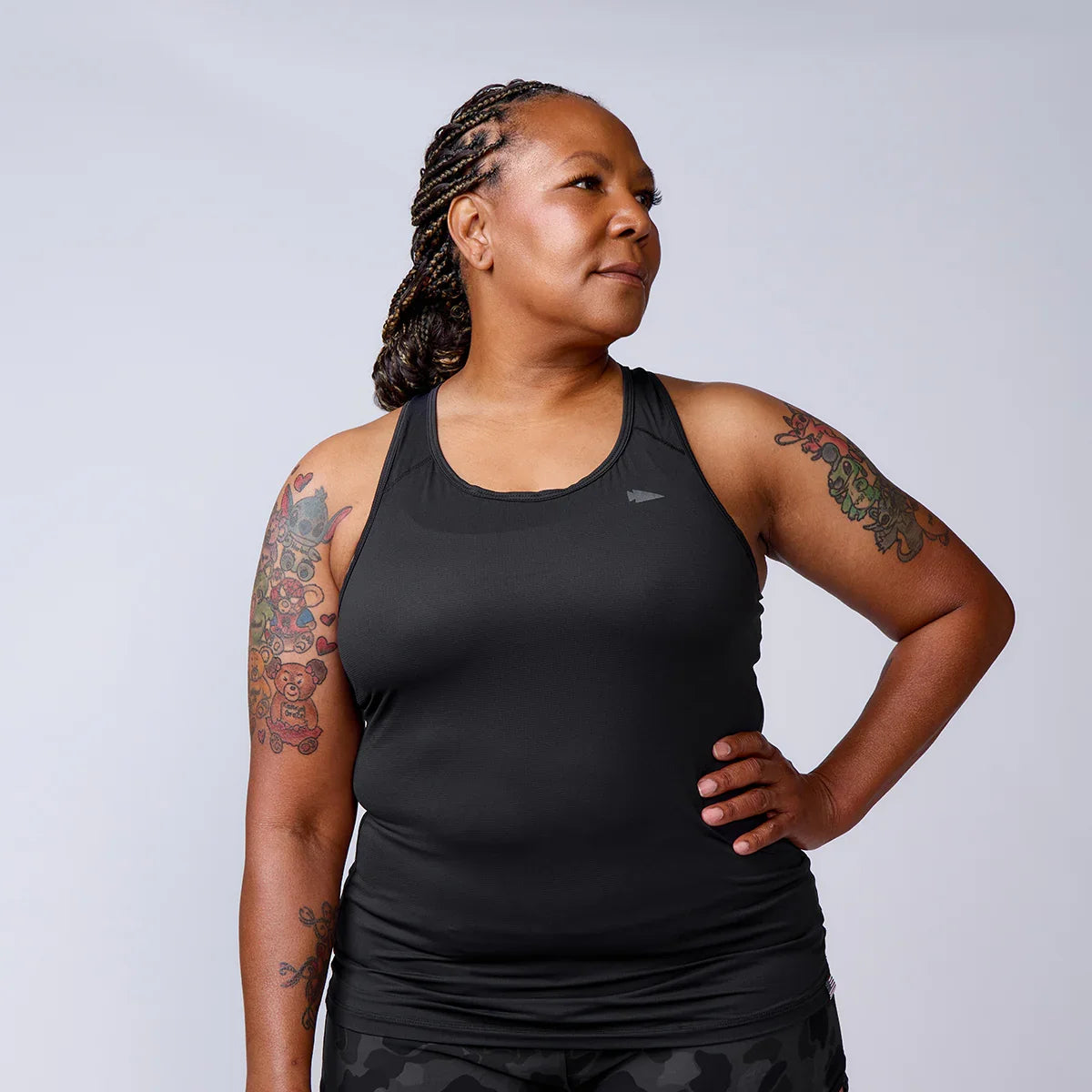Woman in GORUCK black athletic tank top with arm tattoos, standing confidently in studio