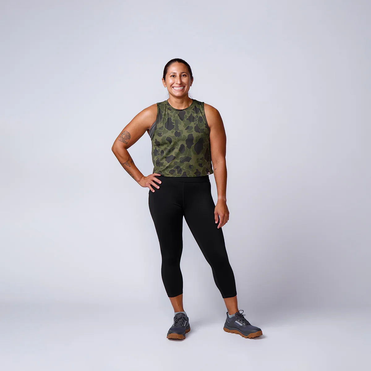 Woman in athletic camo tank top and black leggings, modeling GORUCK rucking gear studio shot