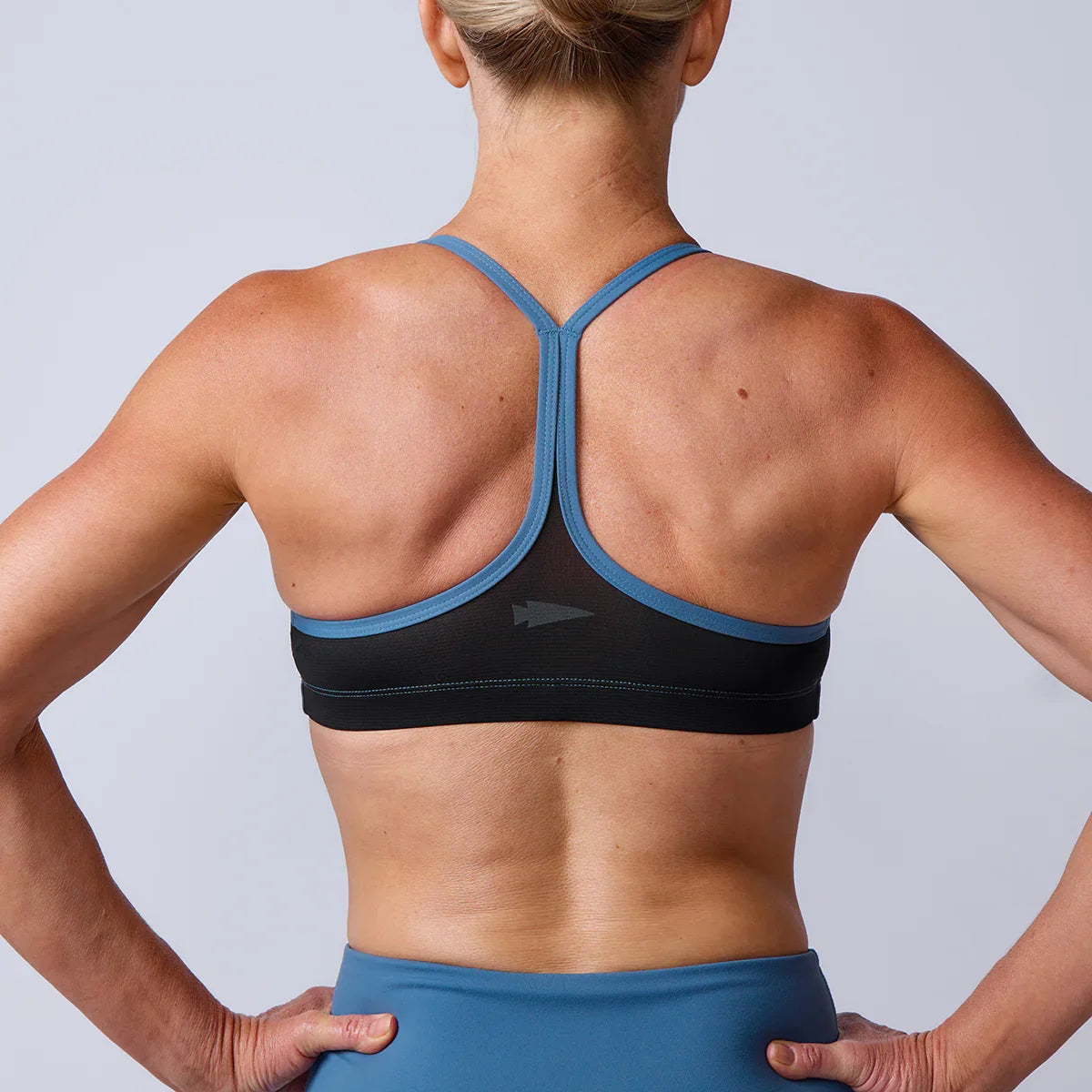 Rear view of fit woman wearing blue and black sports bra and blue workout leggings against gray background