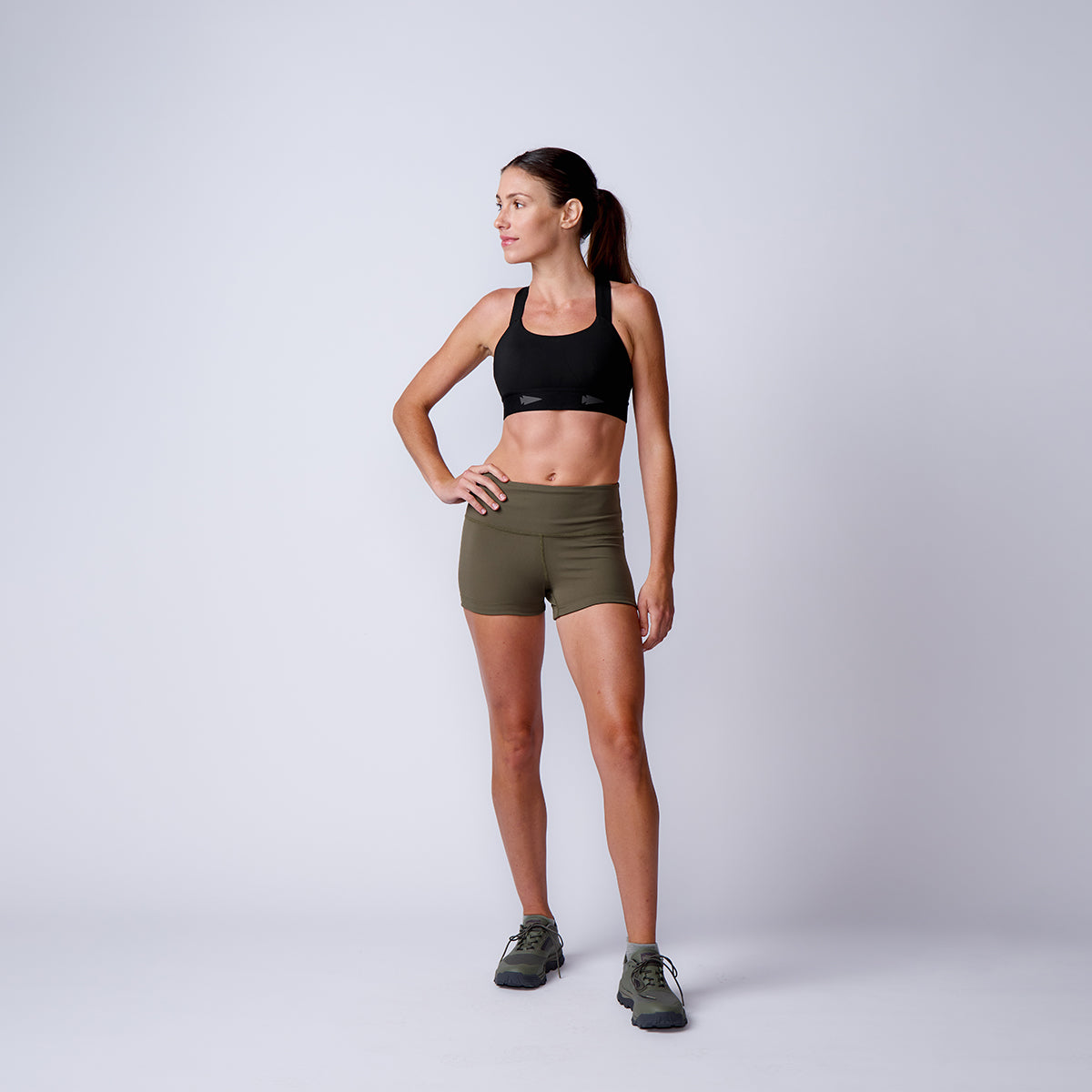A woman confidently stands against a plain background, wearing Women’s Squat Shorts - ToughFlex, featuring a high-waisted design.