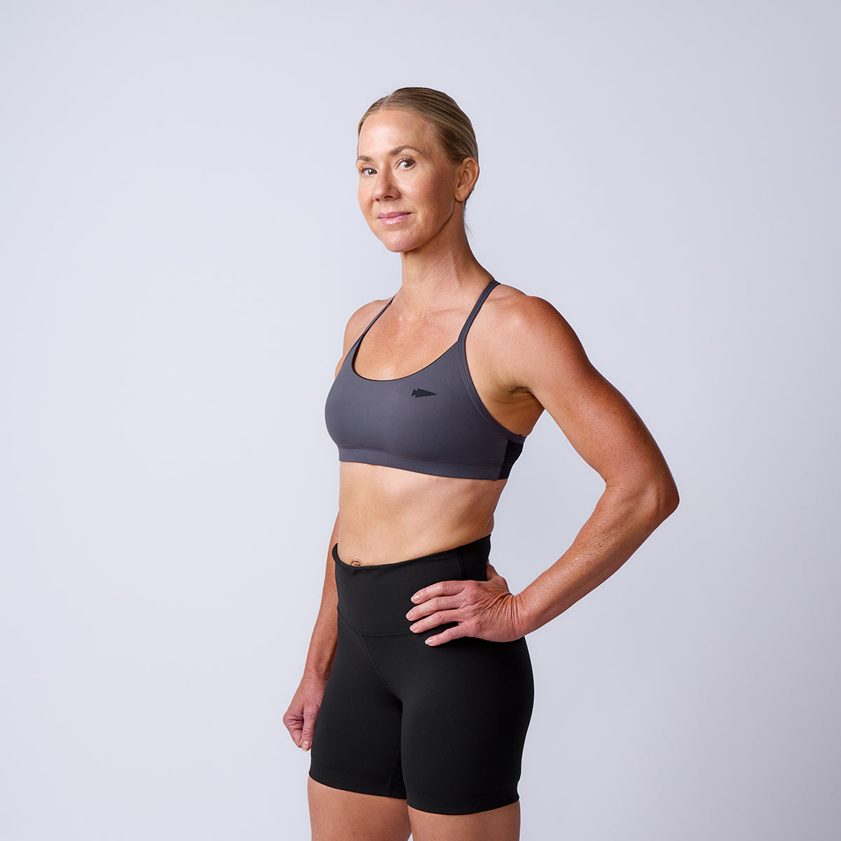A woman in the Stealth Bra - ToughFlex and black shorts stands confidently against a plain light background, highlighting its lightweight support and effortless style.