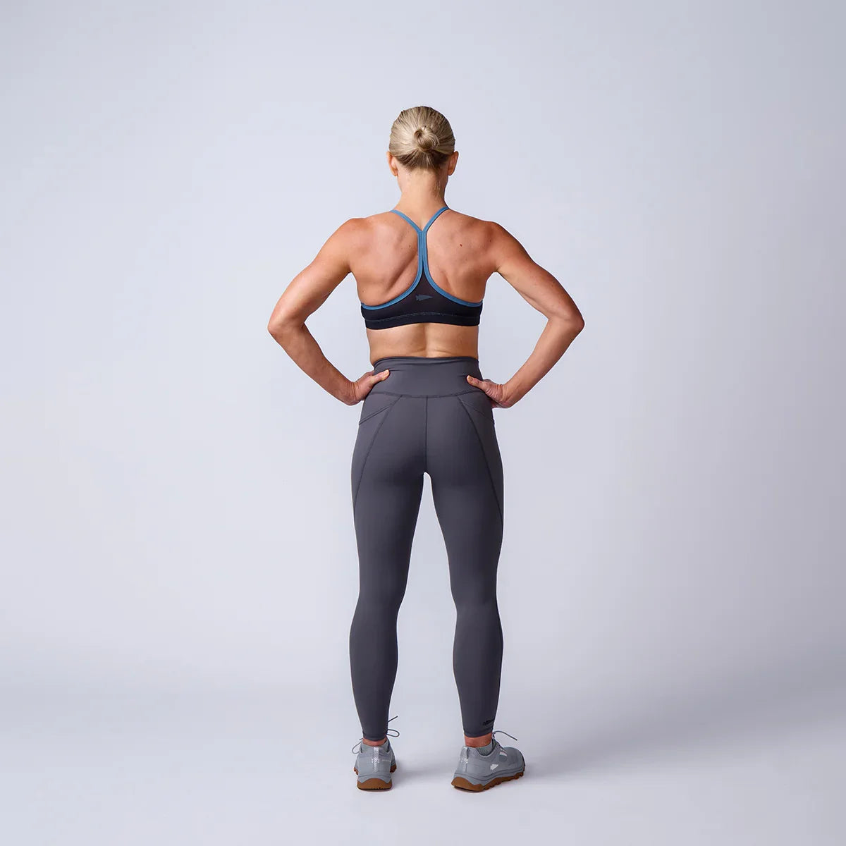 Woman wearing GORUCK athletic sports bra and leggings, standing in studio, back view