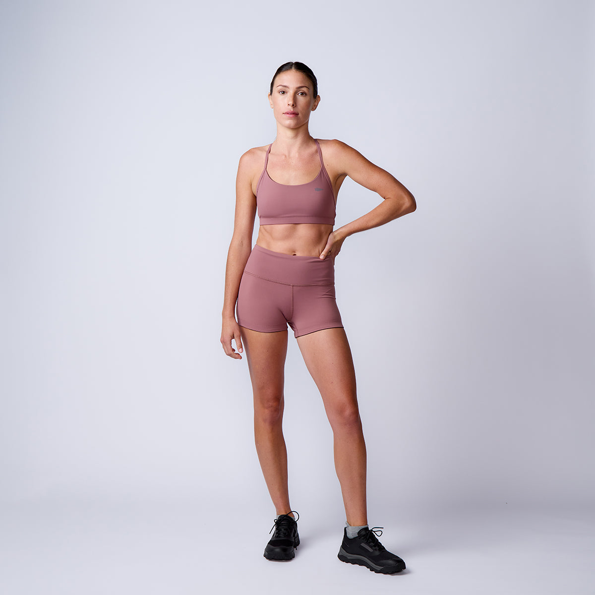 Woman wearing mauve ToughFlex Women’s Squat Shorts and a sports bra stands with one hand on her hip against a plain background.