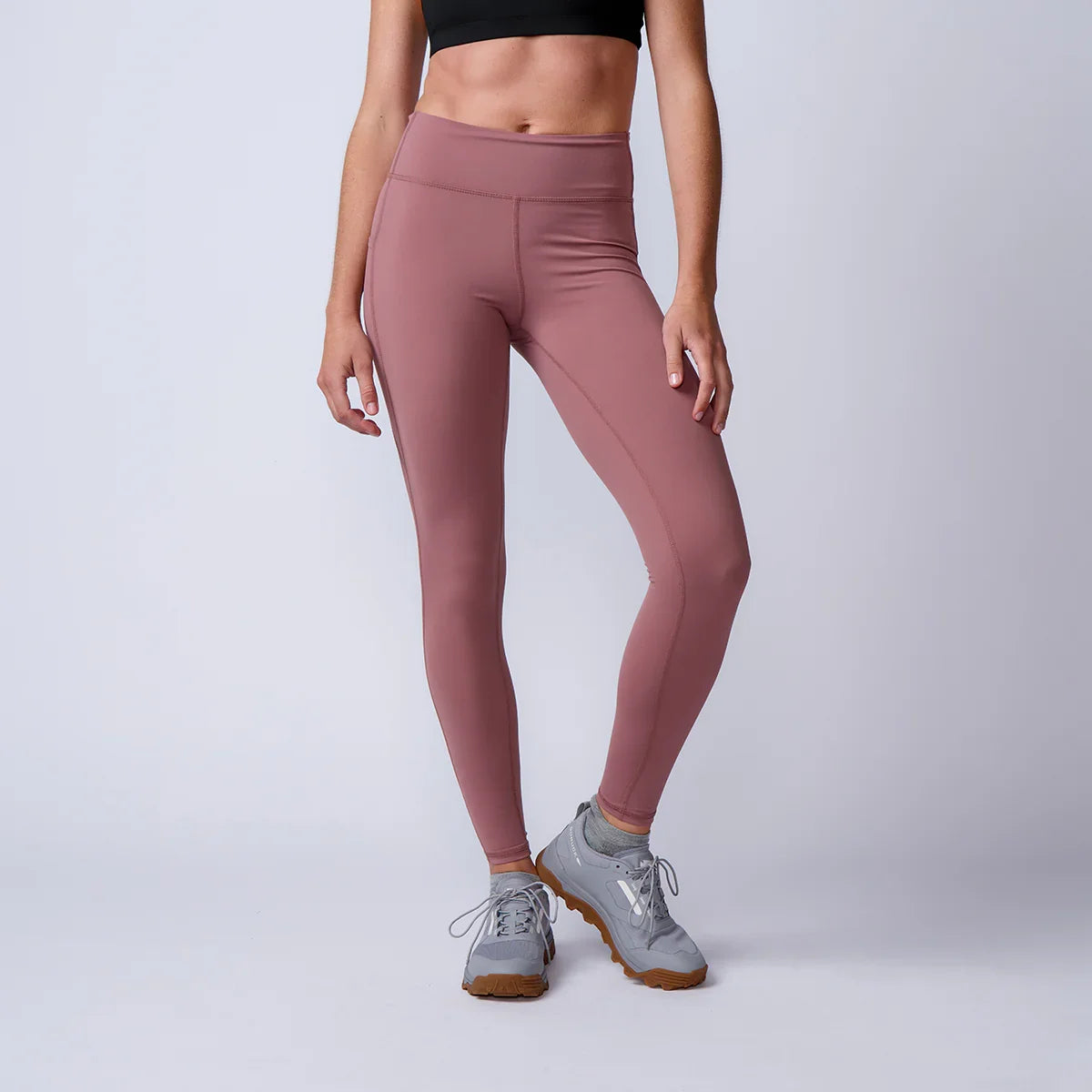 Athletic woman wearing mauve workout leggings and gray sneakers against a plain light background